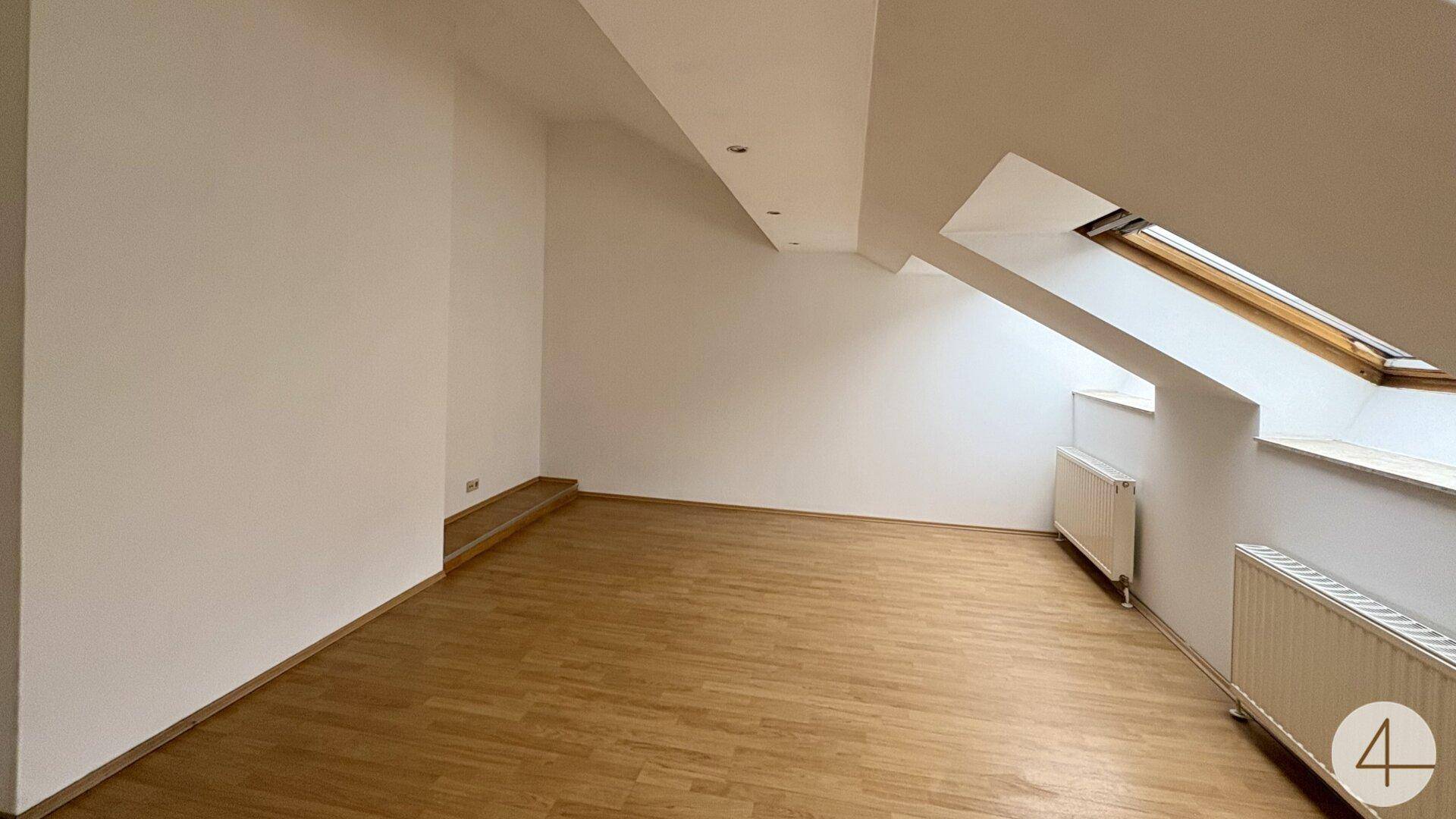 Geräumiges Dachgeschosszimmer mit Holzboden und schrägen Wänden, ideal für Wohnzwecke.