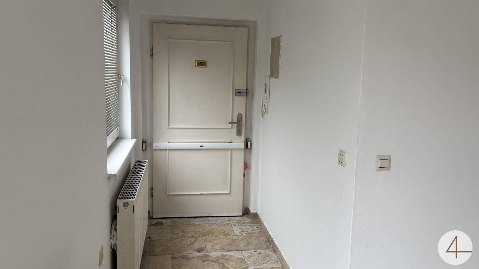 Eingangsbereich mit Fliesenboden, Fenster und einer stabilen Eingangstür.