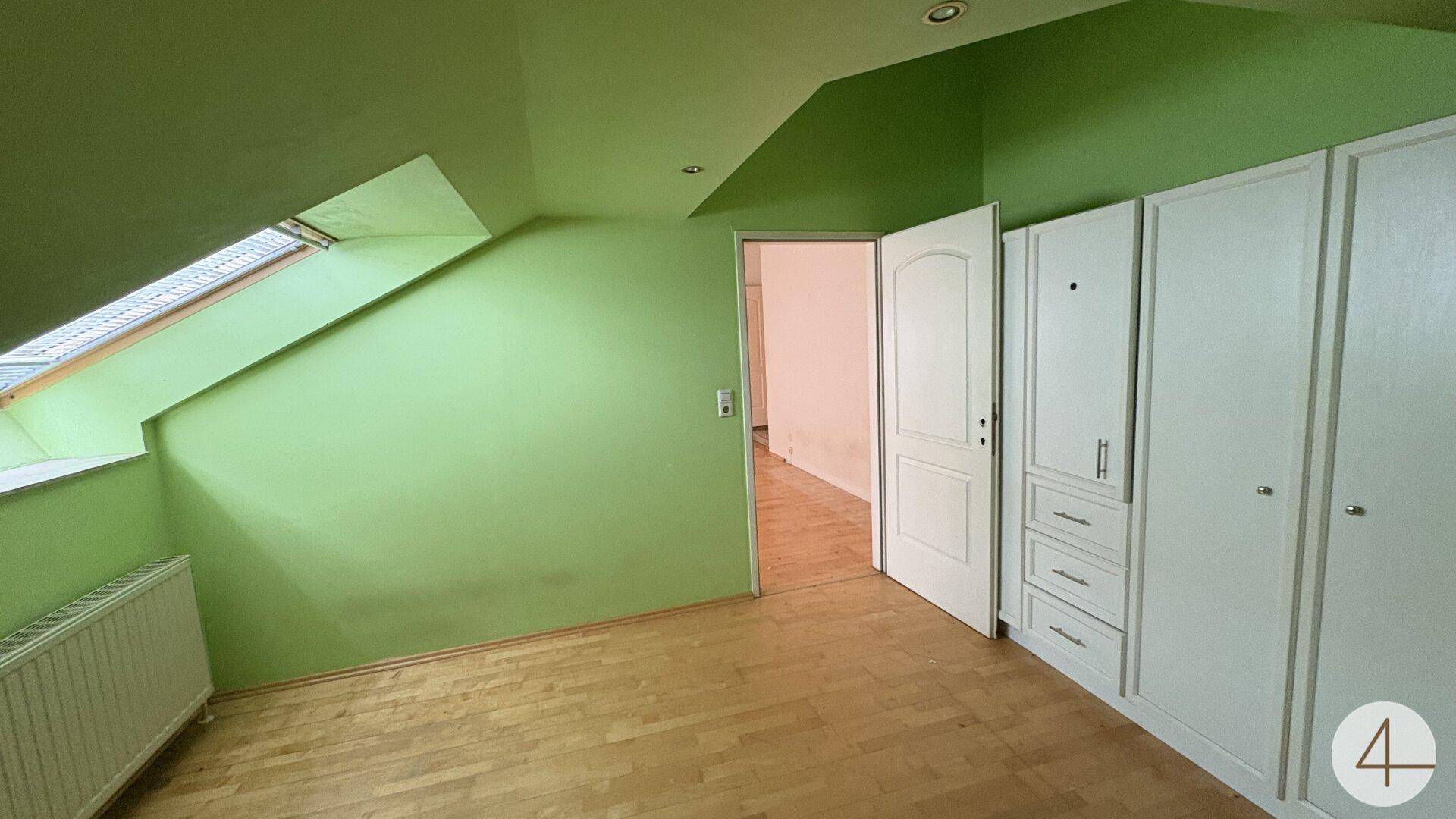 Grünes Schlafzimmer mit Einbauschränken, Dachschräge und Holzfußboden.