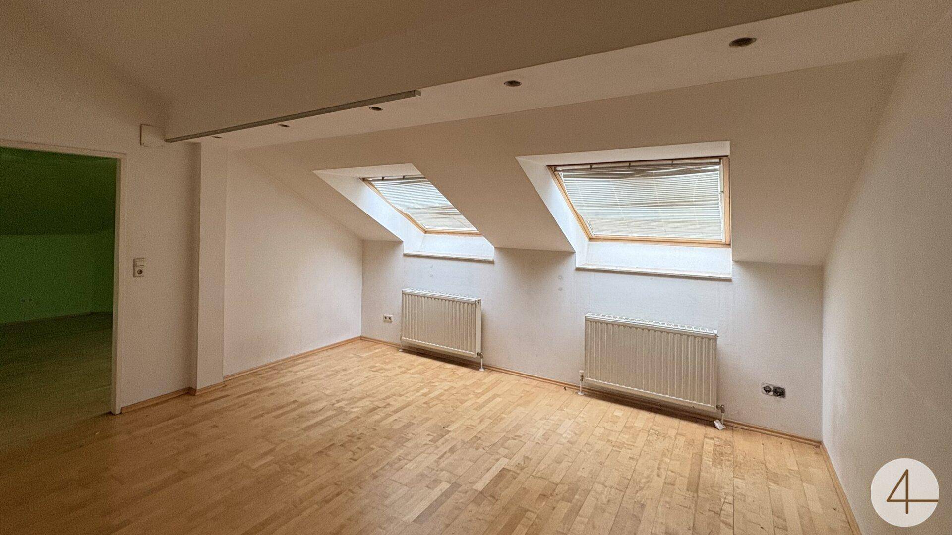 Geräumiges Dachzimmer mit zwei Dachfenstern, Heizkörpern und Holzparkett.