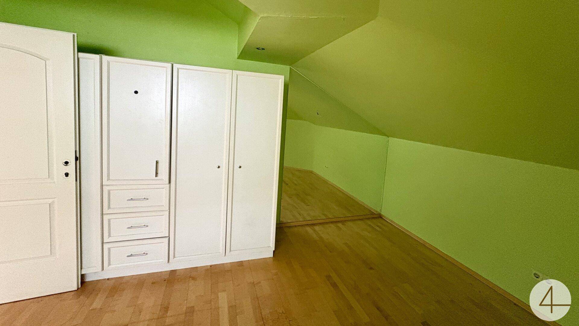 Schlafzimmer mit grünen Wänden, Einbauschränken und schrägem Dach.