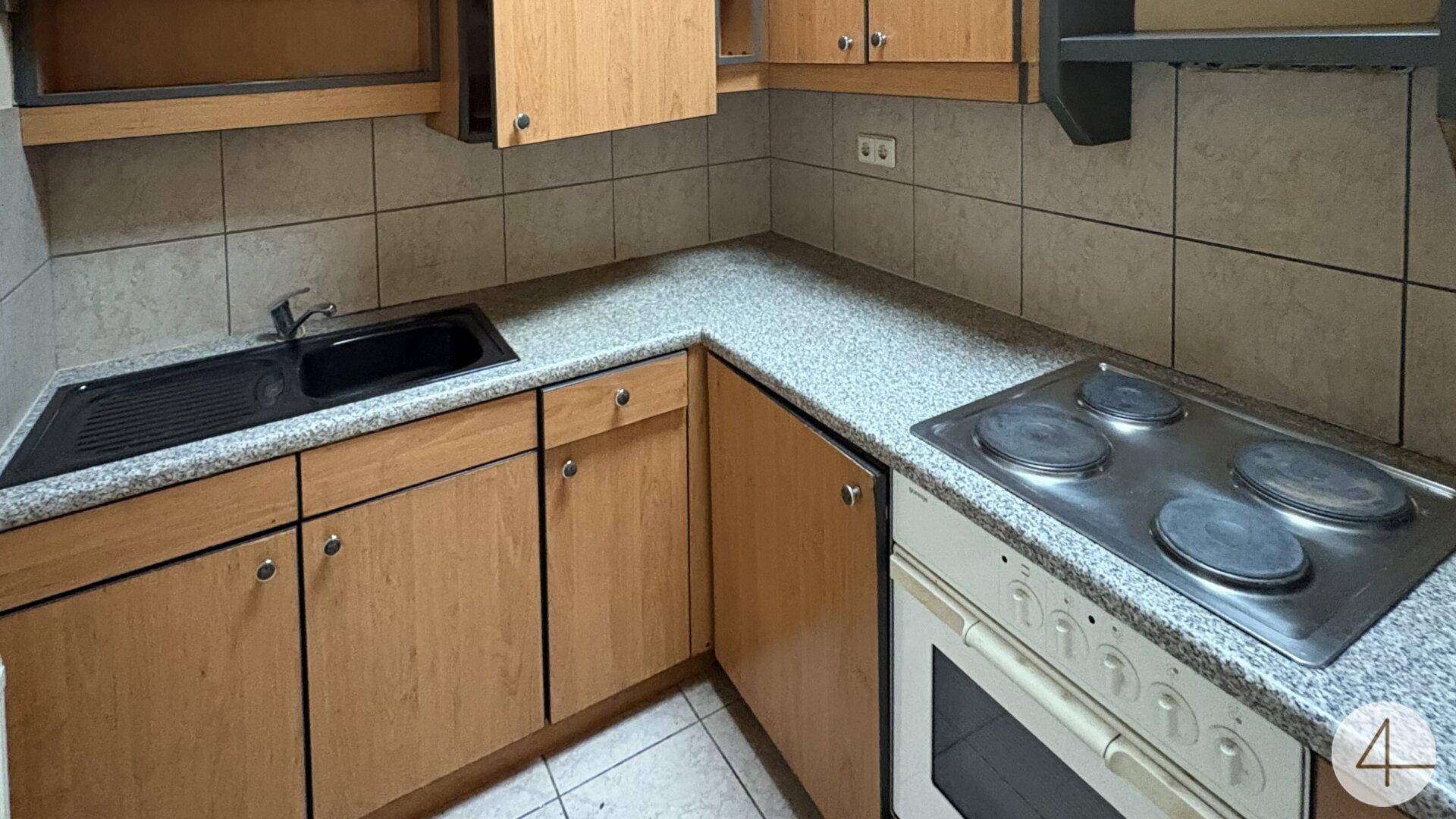 Kompakte Küche mit Holzfronten, gefliestem Boden und Elektroherd.