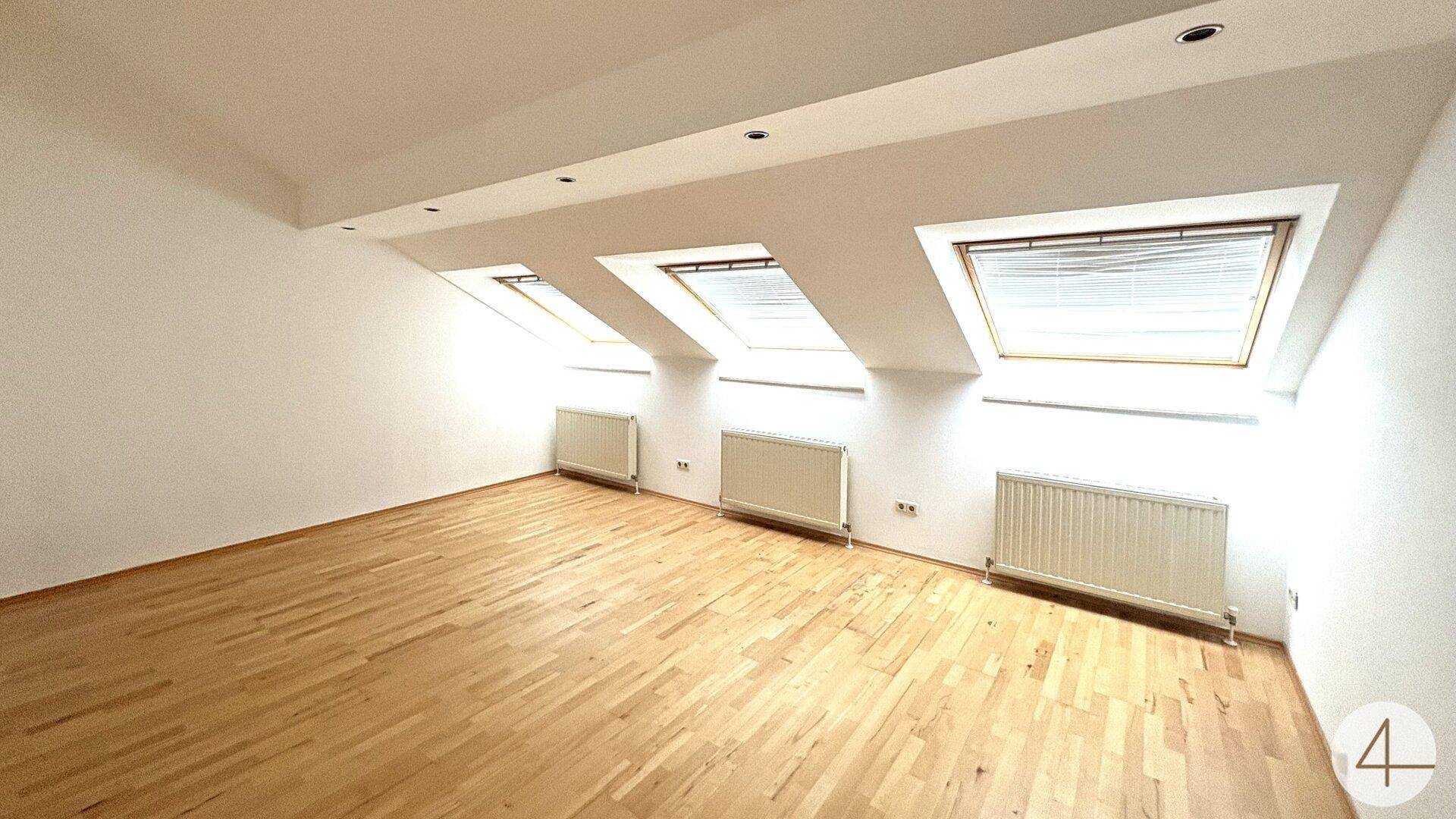 Lichtdurchflutetes Dachzimmer mit drei Dachfenstern und Holzfußboden.