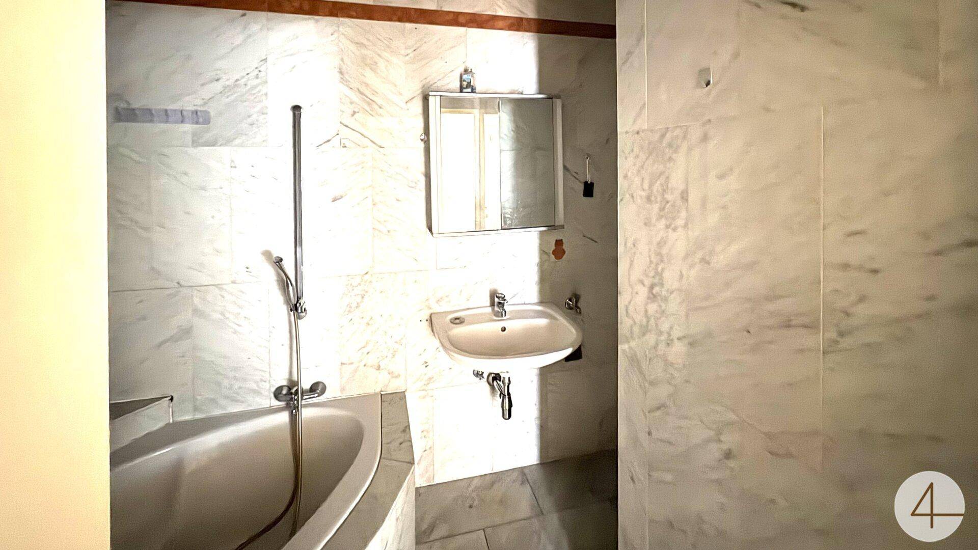 Badezimmer mit Marmorfliesen, Badewanne und Waschbecken.