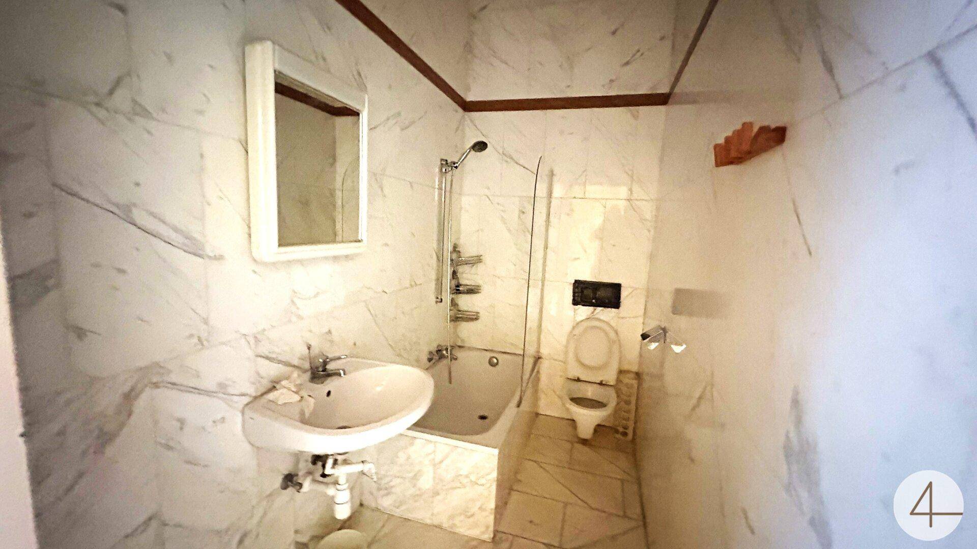 Badezimmer mit Marmorfliesen, Badewanne mit Duschfunktion und Toilette.