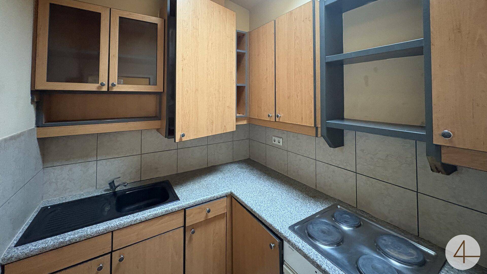 Kleine Küche mit Holzschränken, Fliesenrückwand und Elektroherd.