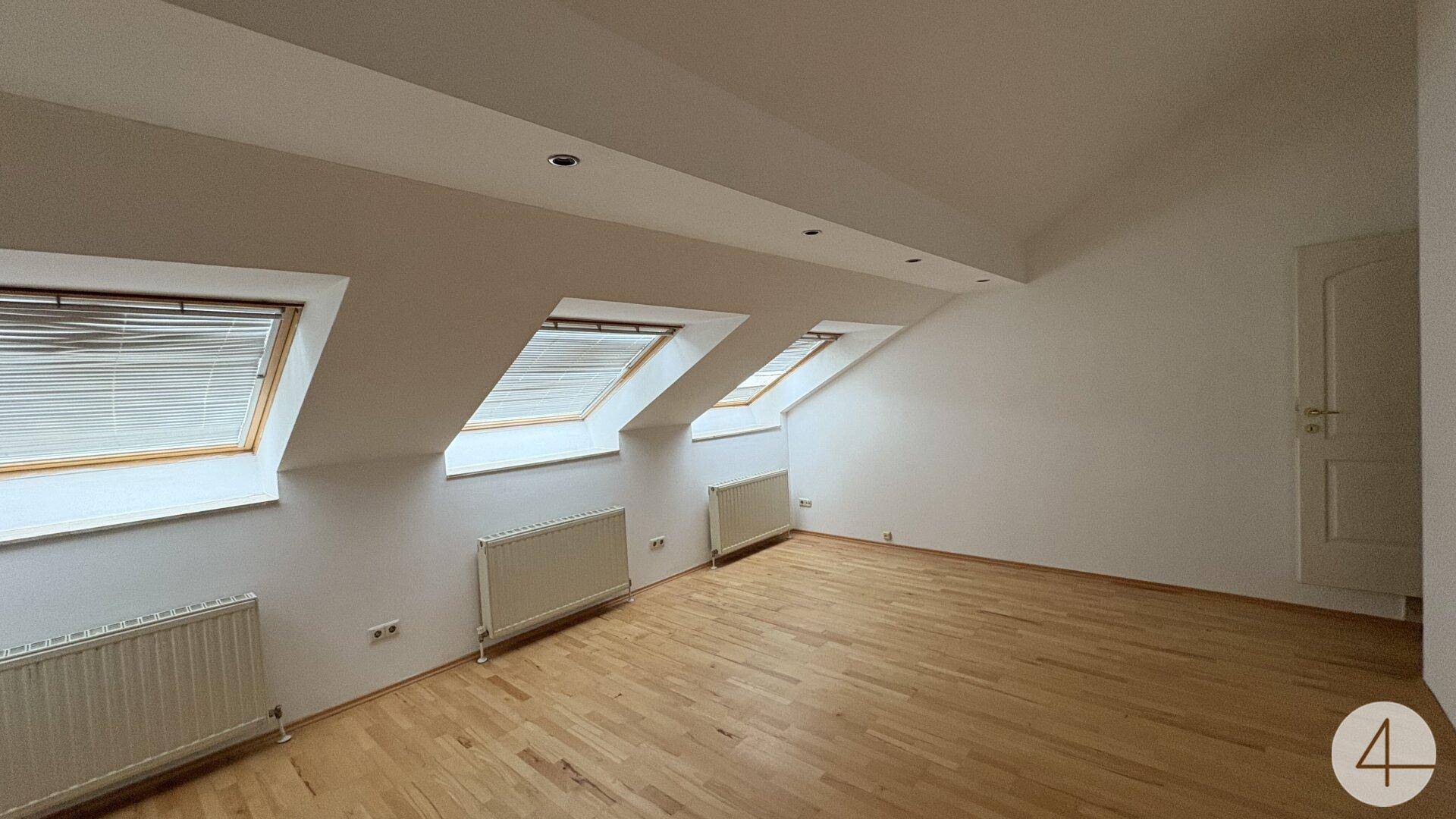 Geräumiges Dachgeschosszimmer mit Holzboden, Dachschrägen und weißer Tür, bietet vielseitige Nutzungsmöglichkeiten.