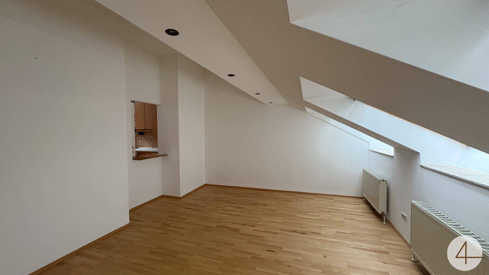 Heller Wohnbereich im Dachgeschoss mit Parkettboden und praktischer Durchreiche zur angrenzenden Küche.