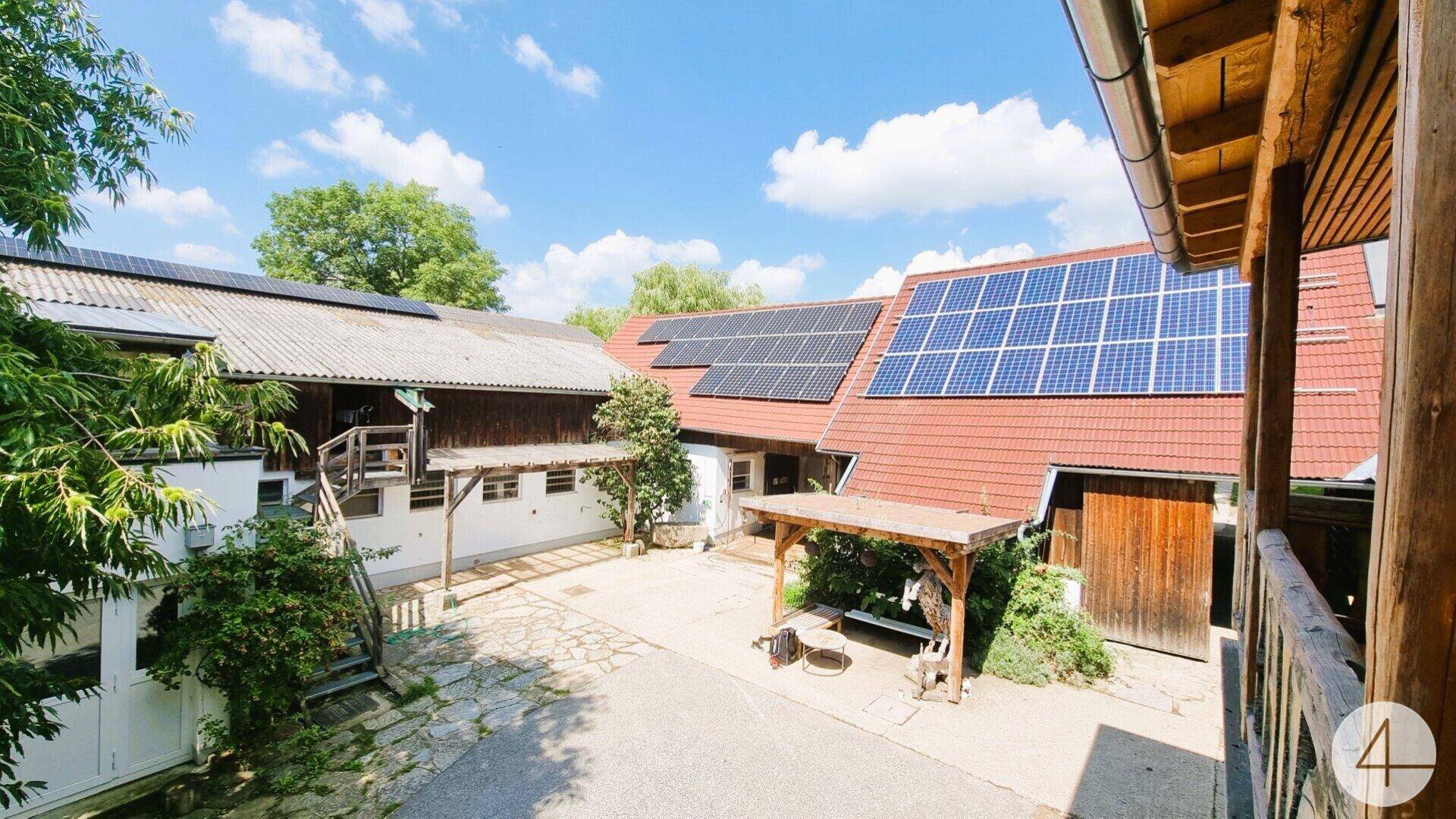 Bauernhofanlage mit mehreren Gebäuden, roten Dächern und Photovoltaikanlagen unter blauem Himmel.