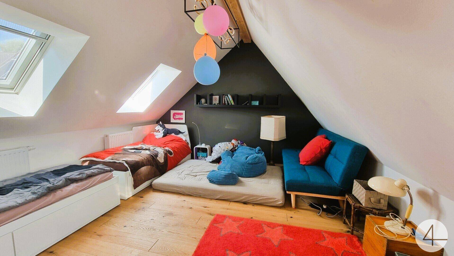 Helles Kinderzimmer mit Dachschrägen, Dachfenstern und Holzboden, farbenfroh eingerichtet.