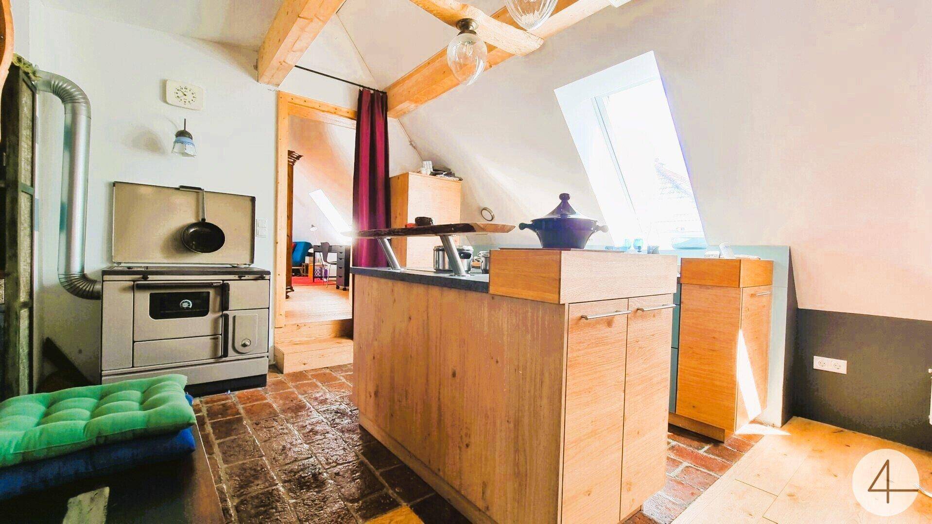 Rustikale Küche mit Holzofen, Kücheninsel und Dachschräge, mit Terrakottafliesen.