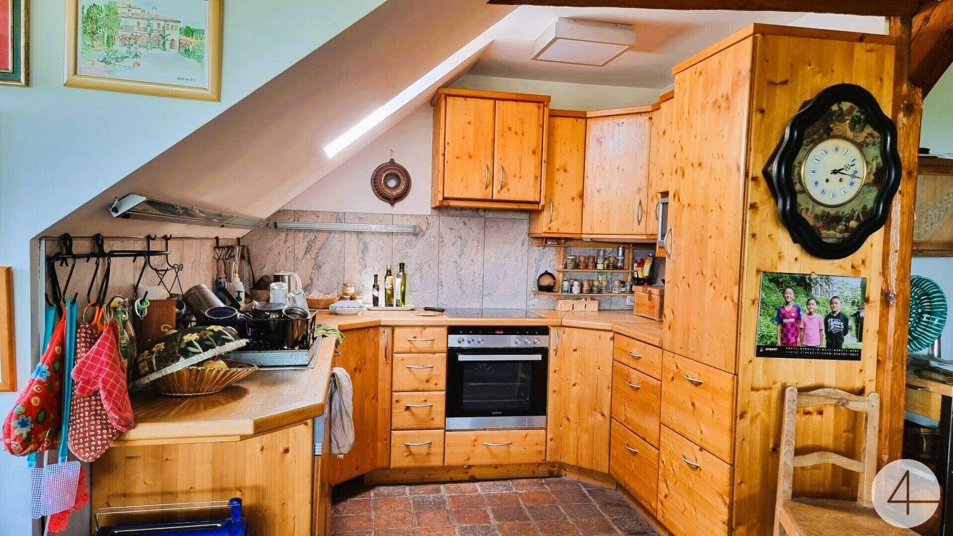 Gemütliche Holzküche mit Dachschräge, Einbaugeräten und Terrakottafliesen, im Landhausstil.