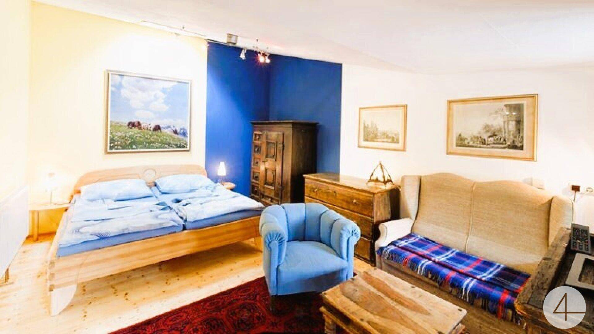 Helles Schlafzimmer mit Holzboden, Doppelbett und blauer Akzentwand, gemütlich eingerichtet.