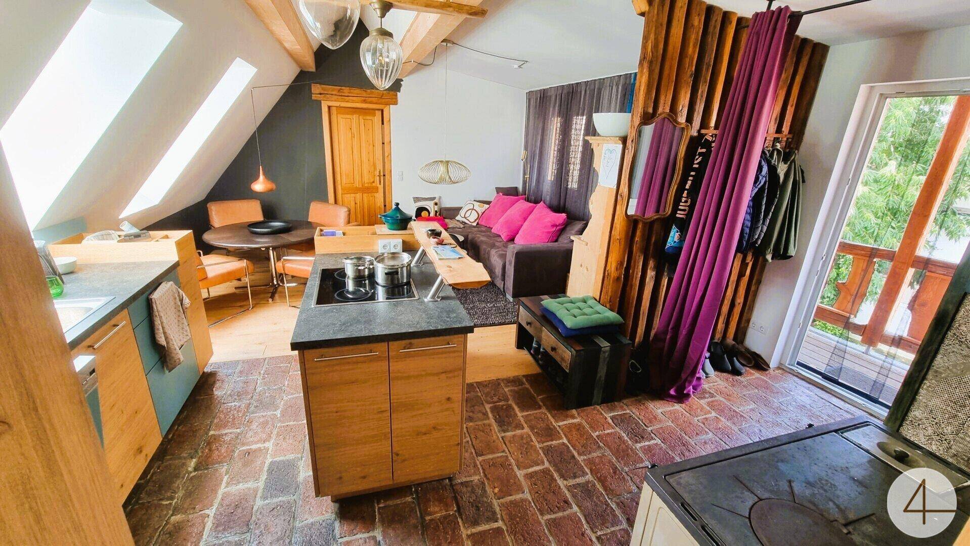 Offener Wohnbereich mit Kücheninsel, Dachschrägen und Zugang zu einem Balkon, hell und geräumig.