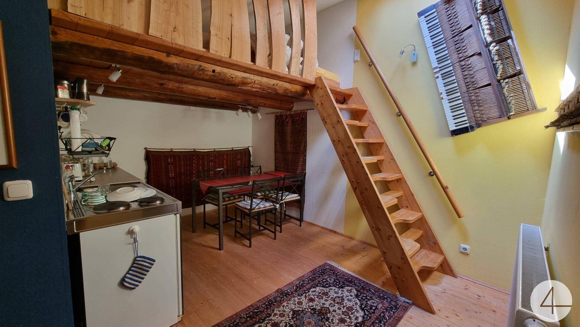 Kleiner Wohnbereich mit Küchenzeile, Esstisch und Holztreppe zu einer Empore.
