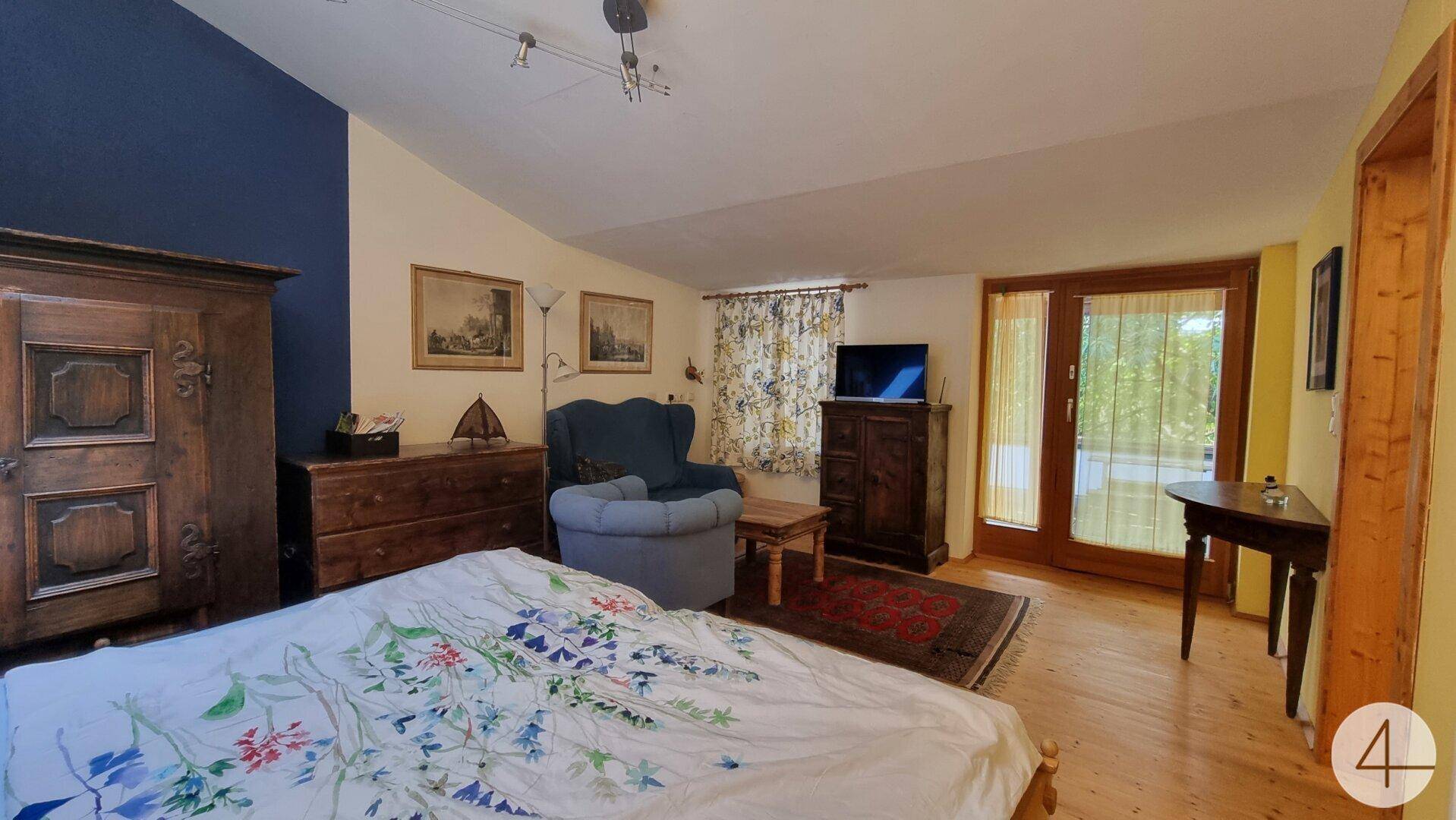 Geräumiges Schlafzimmer mit Holzboden, traditionellen Möbeln und Zugang zu einem Balkon.
