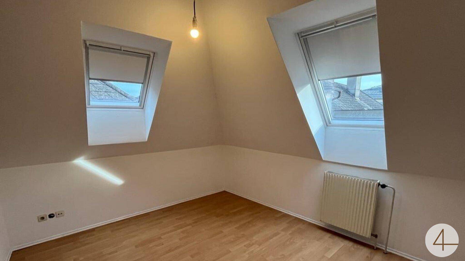 Helles Zimmer im Dachgeschoss mit schrägen Wänden, Holzboden und zwei Dachfenstern.