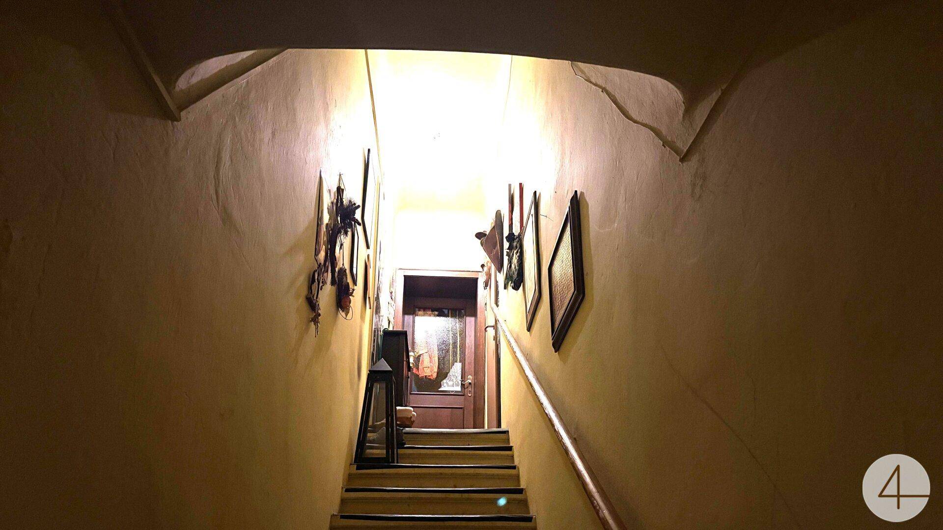 Dunkles Treppenhaus mit gewölbter Decke und Bildern an den Wänden, die nach oben führen.