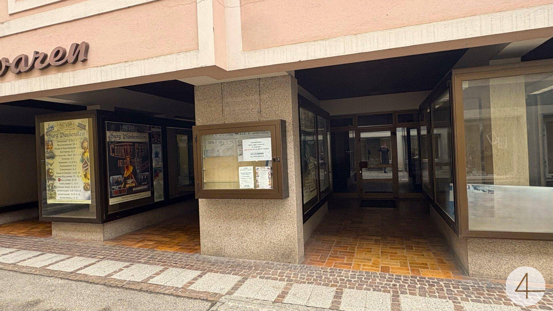 Überdachter Bereich mit Schaufenstern und Informationsvitrinen in einer Ladenpassage.