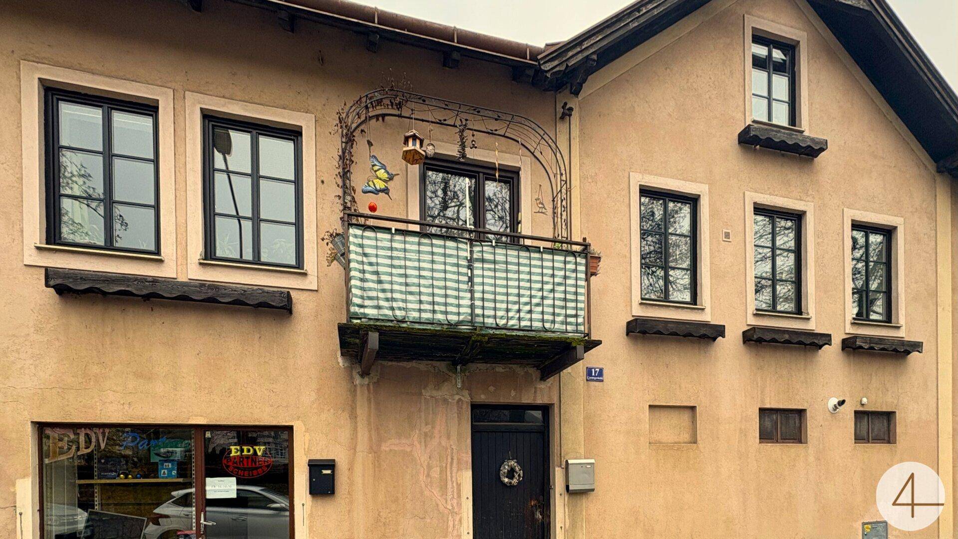 Fassade eines älteren Gebäudes mit einem kleinen Balkon und dunklen Fenstern.