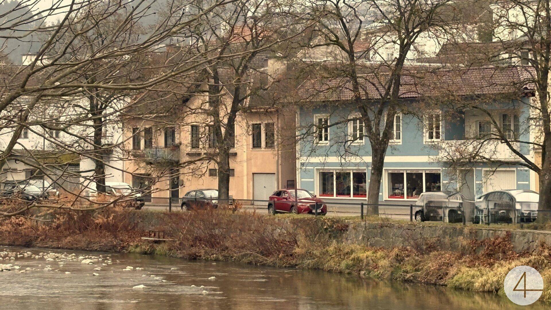 Flussufer mit historischen Gebäuden und kahlen Bäumen in einer städtischen Umgebung.
