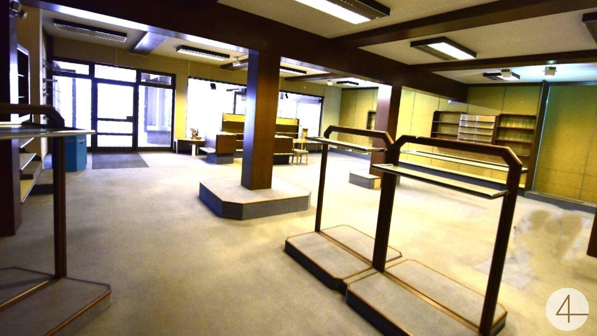 Großer, leerer Ladenraum mit Regalen, Schaufenstern und Teppichboden.