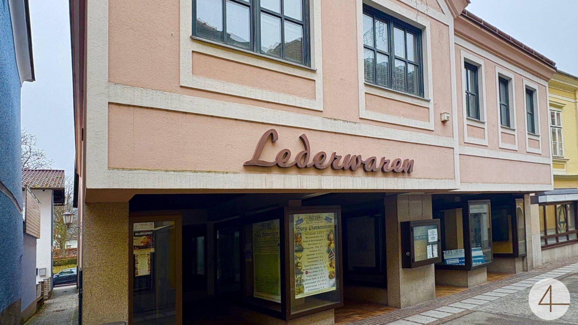 Historisches Gebäude mit Ladenfronten und dem Schriftzug "Lederwaren" in einer Stadtgasse.