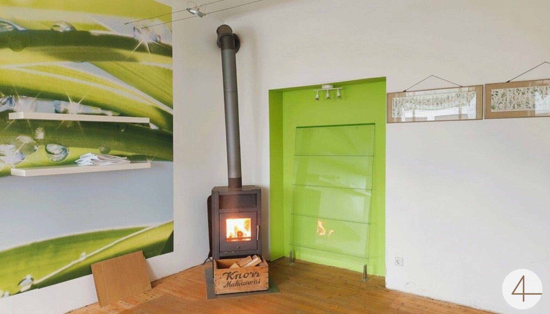 Heller Raum mit Holzboden, modernem Kaminofen und auffälliger grüner Akzentwand.