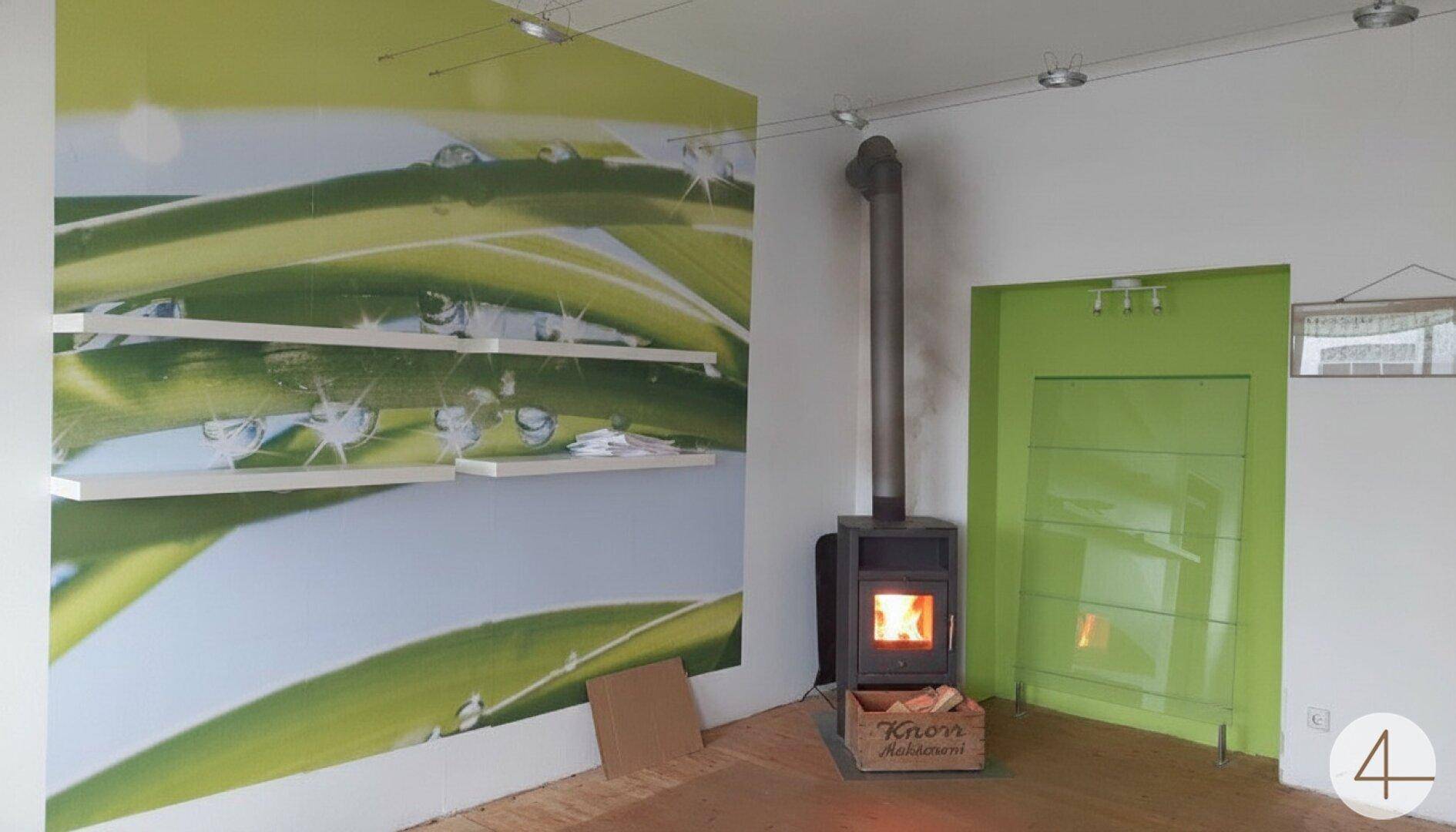 Gemütlicher Wohnbereich mit Kaminofen, Holzboden und einer modernen Glasabtrennung.