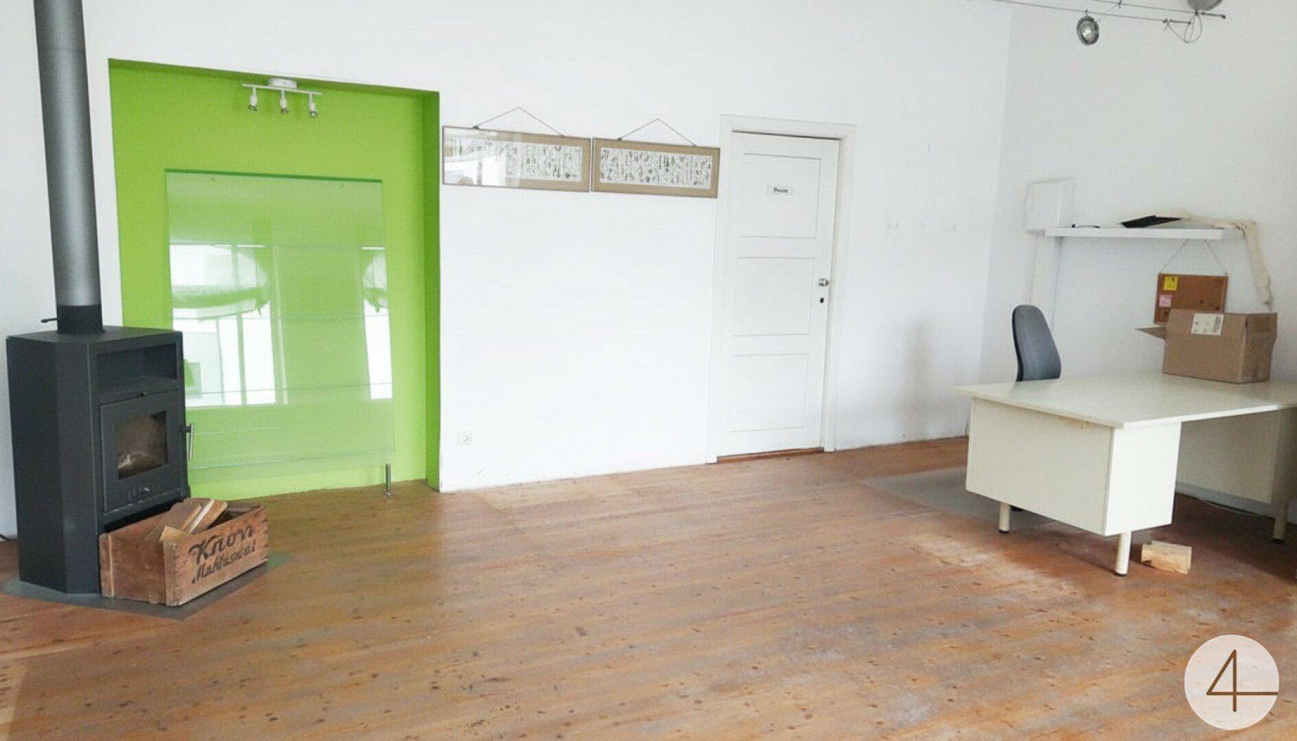 Geräumiger Arbeitsbereich mit Holzboden, Kaminofen und einem Schreibtisch.