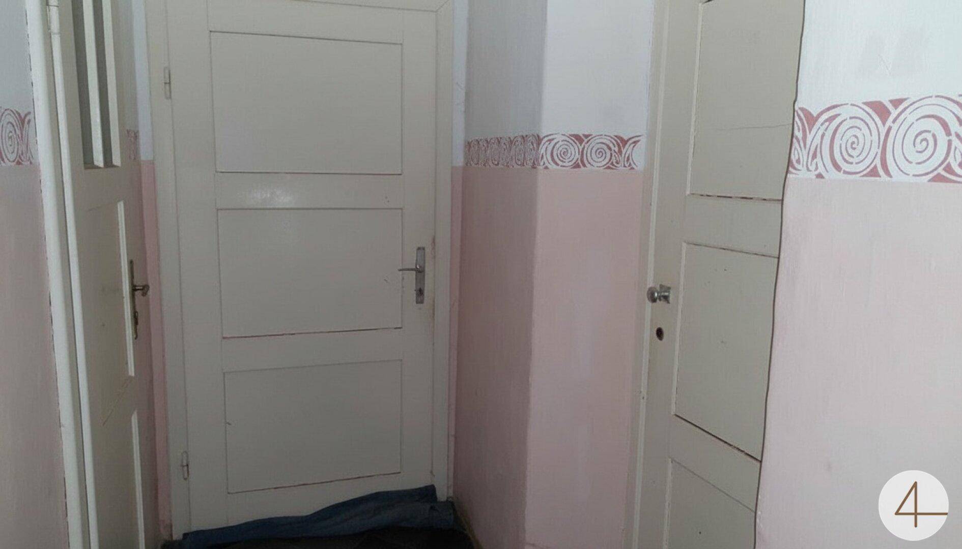 Flur mit weißer Tür und Wänden in Pastellrosa mit dekorativen Mustern.