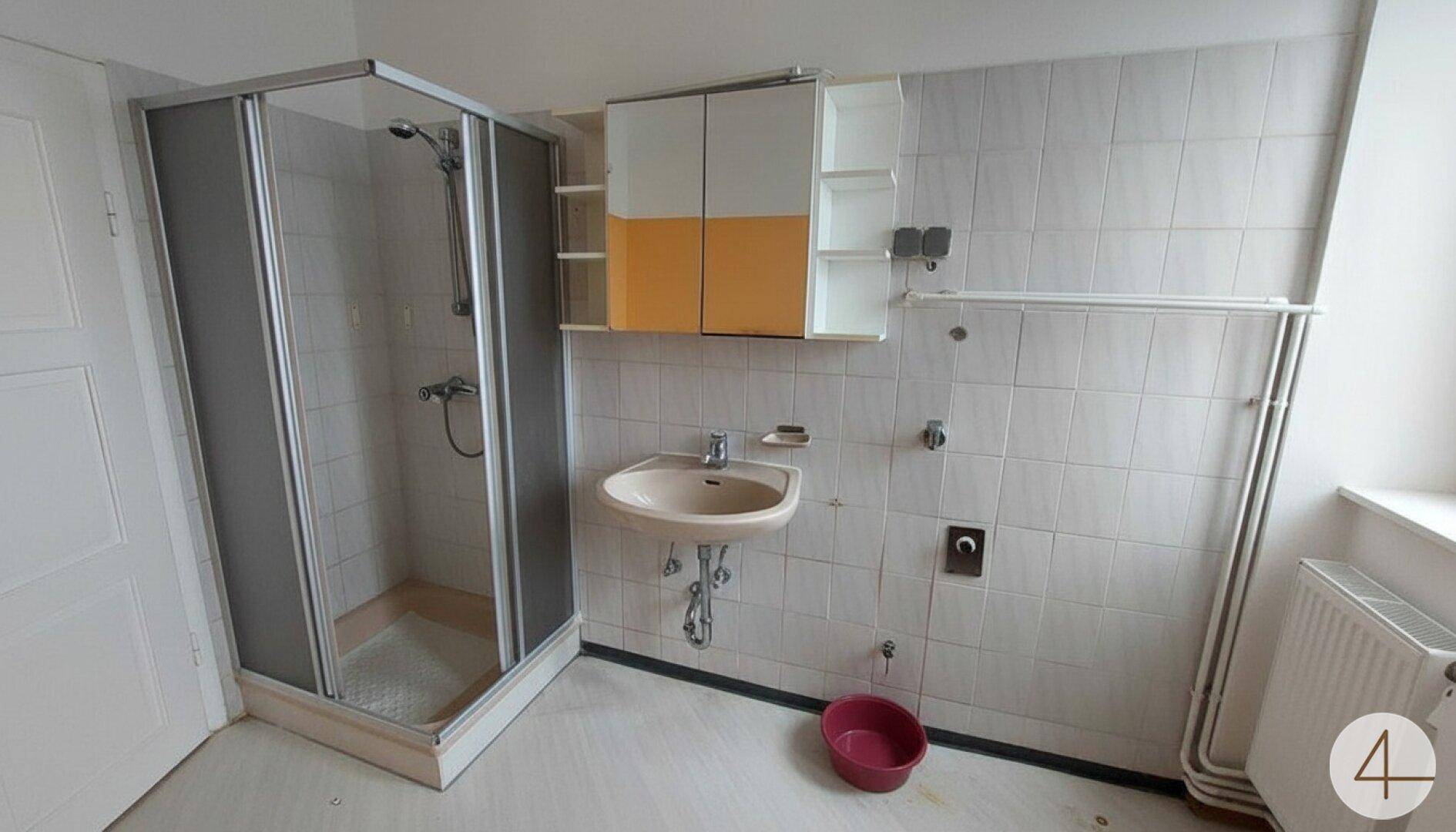 Badezimmer mit Duschkabine, Waschbecken und gefliesten Wänden, das eine Renovierung benötigt.