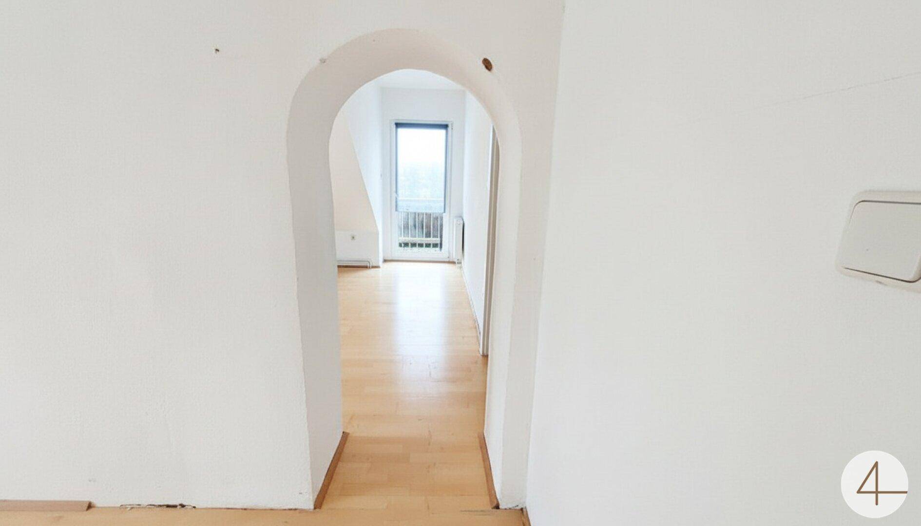 Heller Flur mit Holzboden und einem Rundbogen, der zu einem weiteren Raum führt.