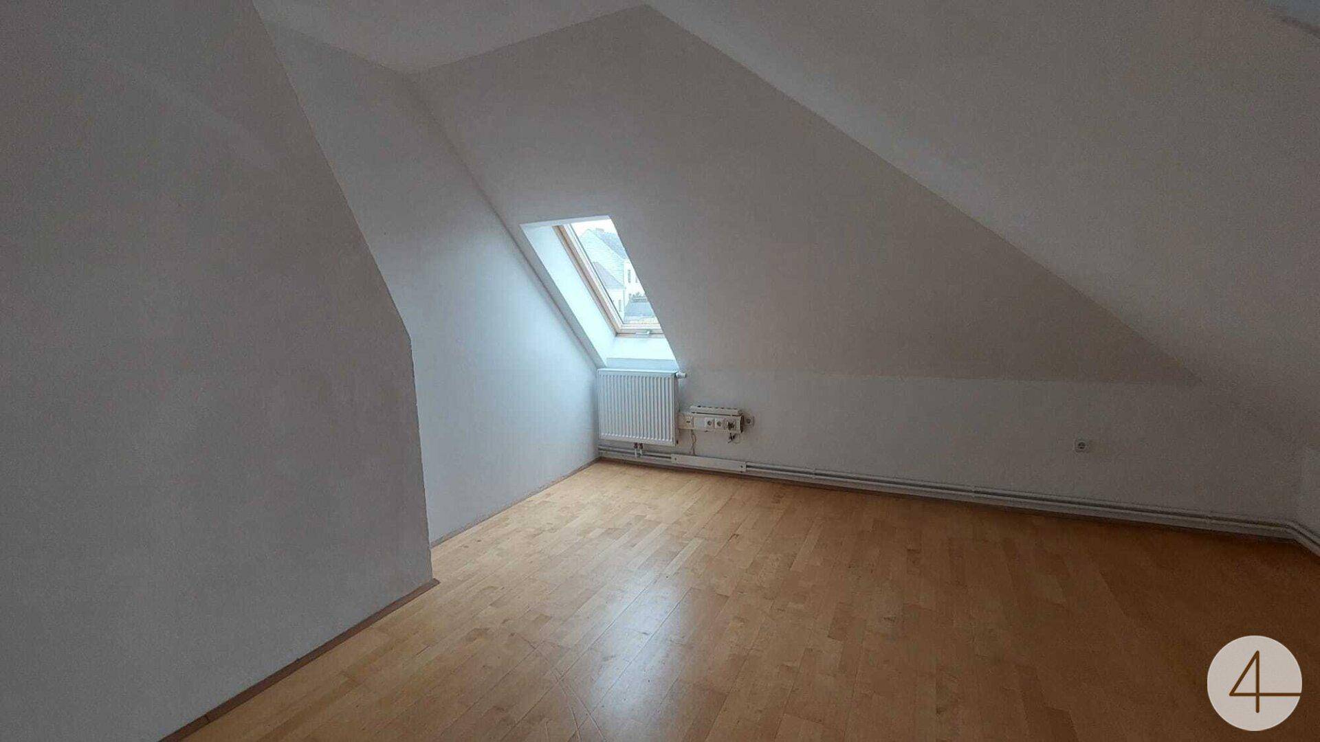 Helles Dachzimmer mit schrägen Wänden, Laminatboden und einem Dachfenster für natürliches Licht.