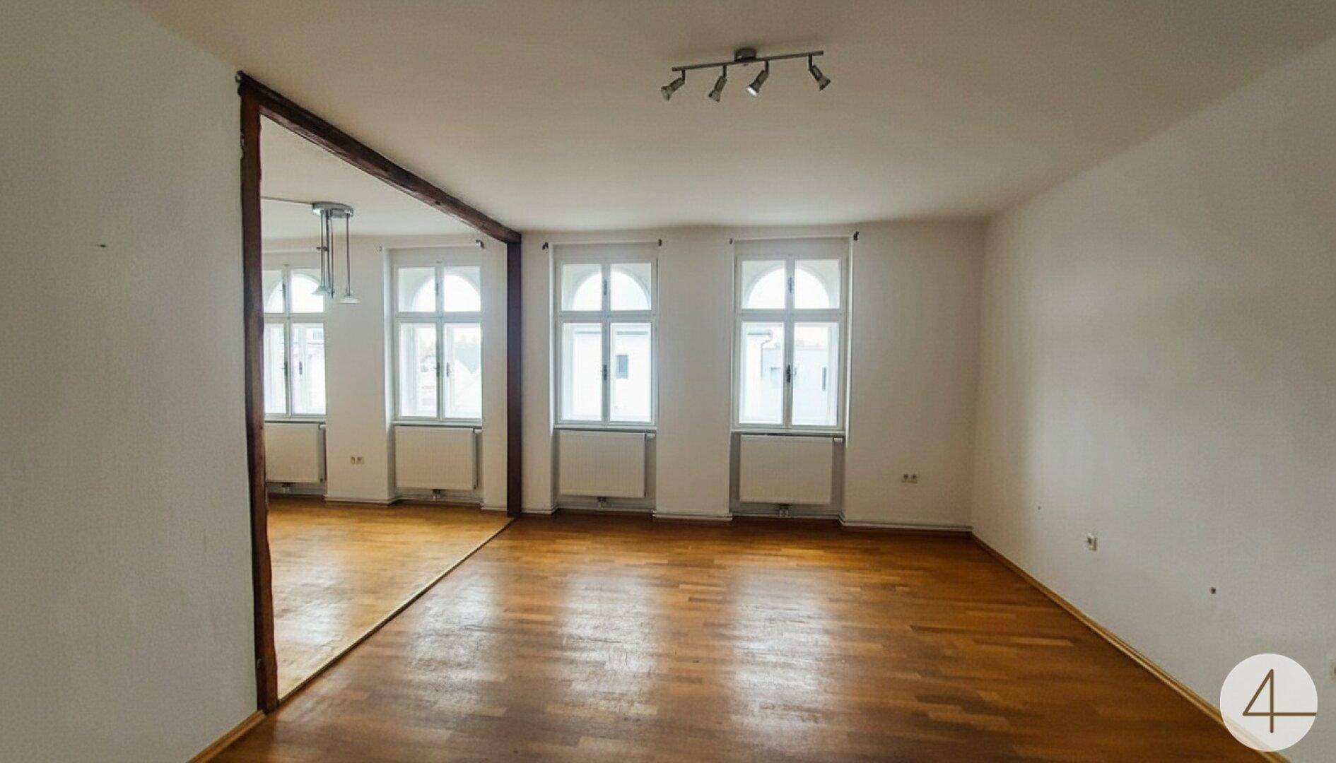Geräumiger, heller Wohnbereich mit Holzboden und mehreren Fenstern, bereit zur individuellen Gestaltung.