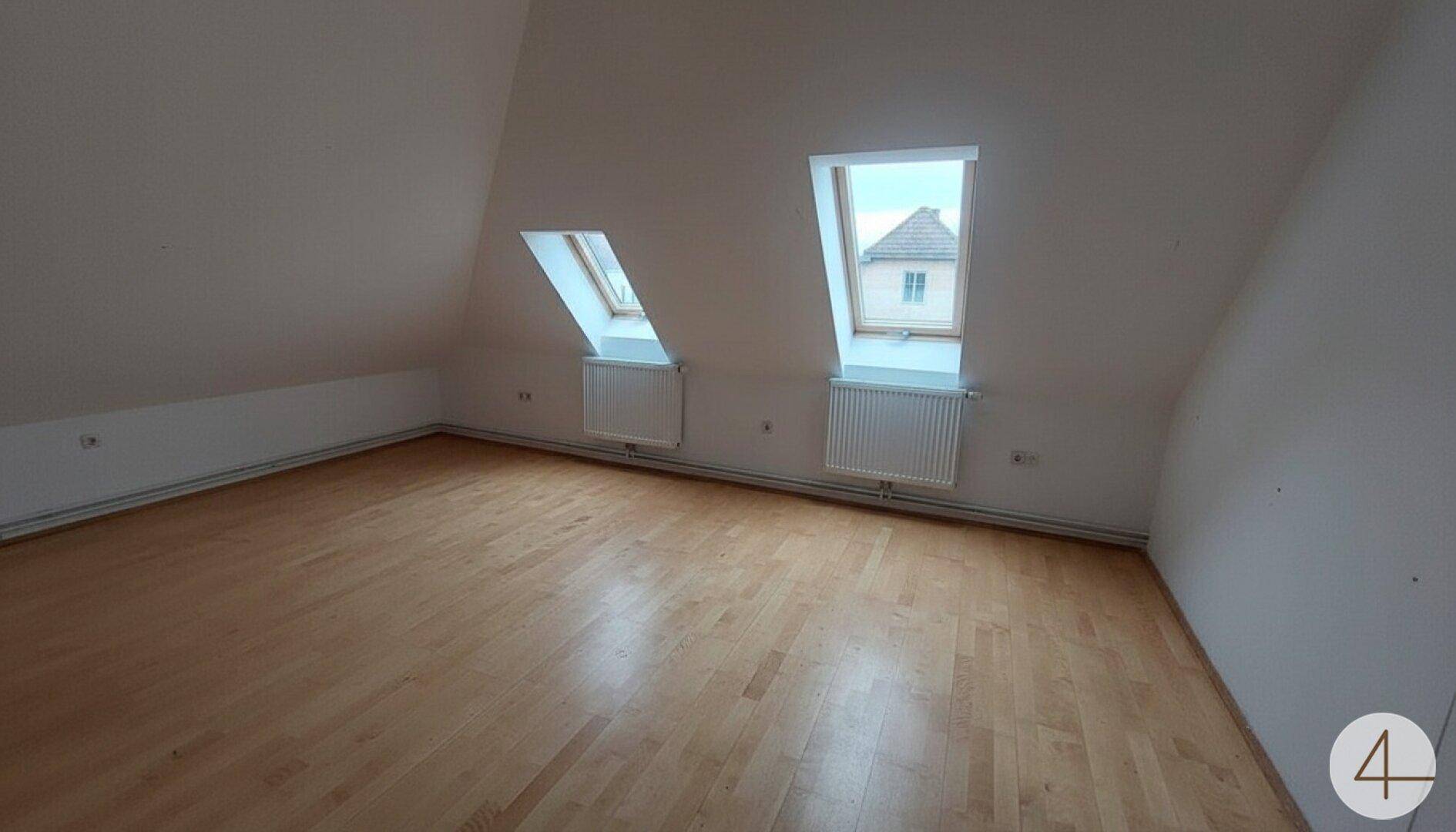 Geräumiges Dachzimmer mit zwei Dachfenstern, Laminatboden und schrägen Wänden, ideal als Schlafzimmer.