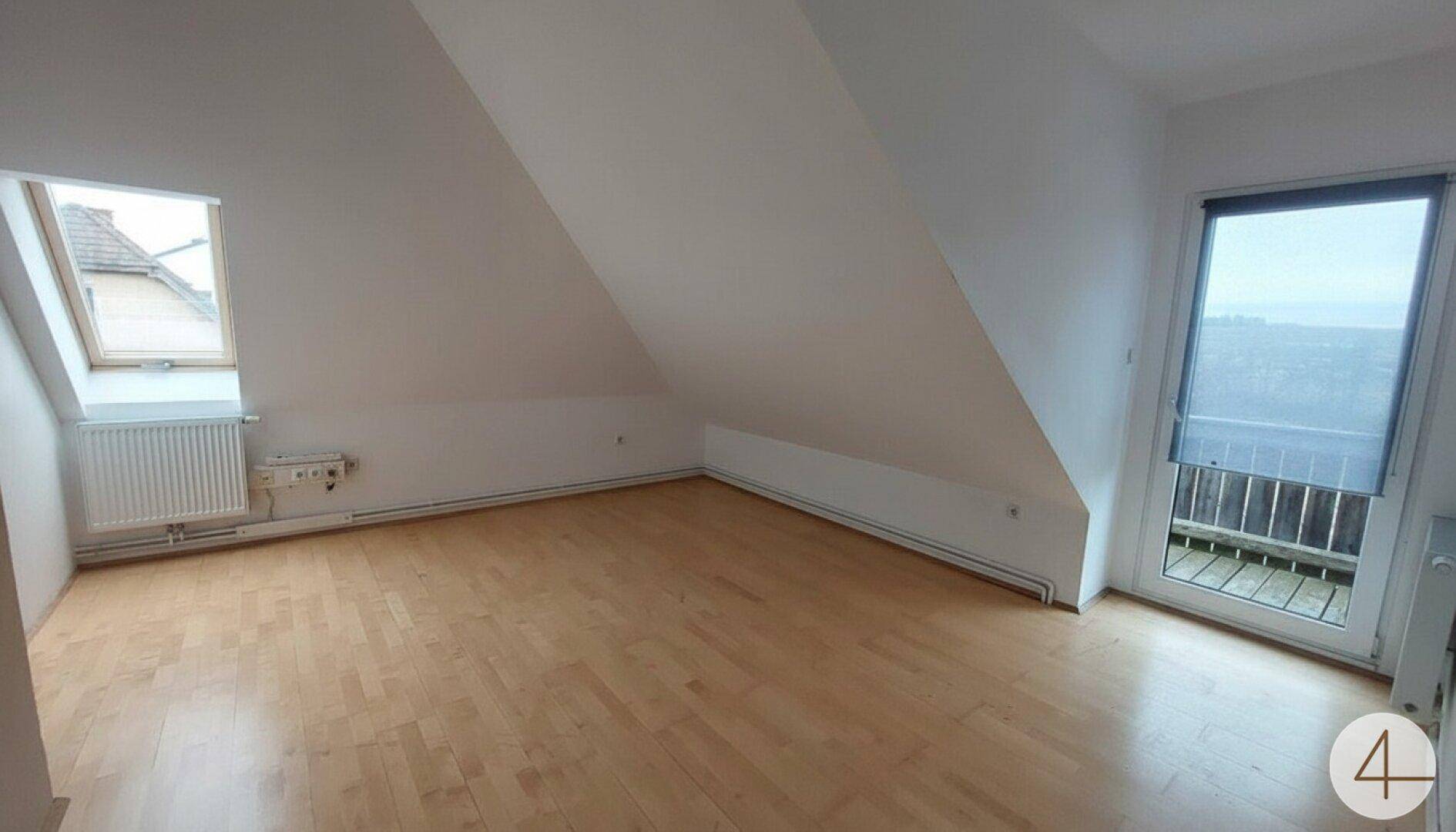 Helles Dachzimmer mit Laminatboden, Dachfenster und Zugang zu einem französischen Balkon mit Weitblick.