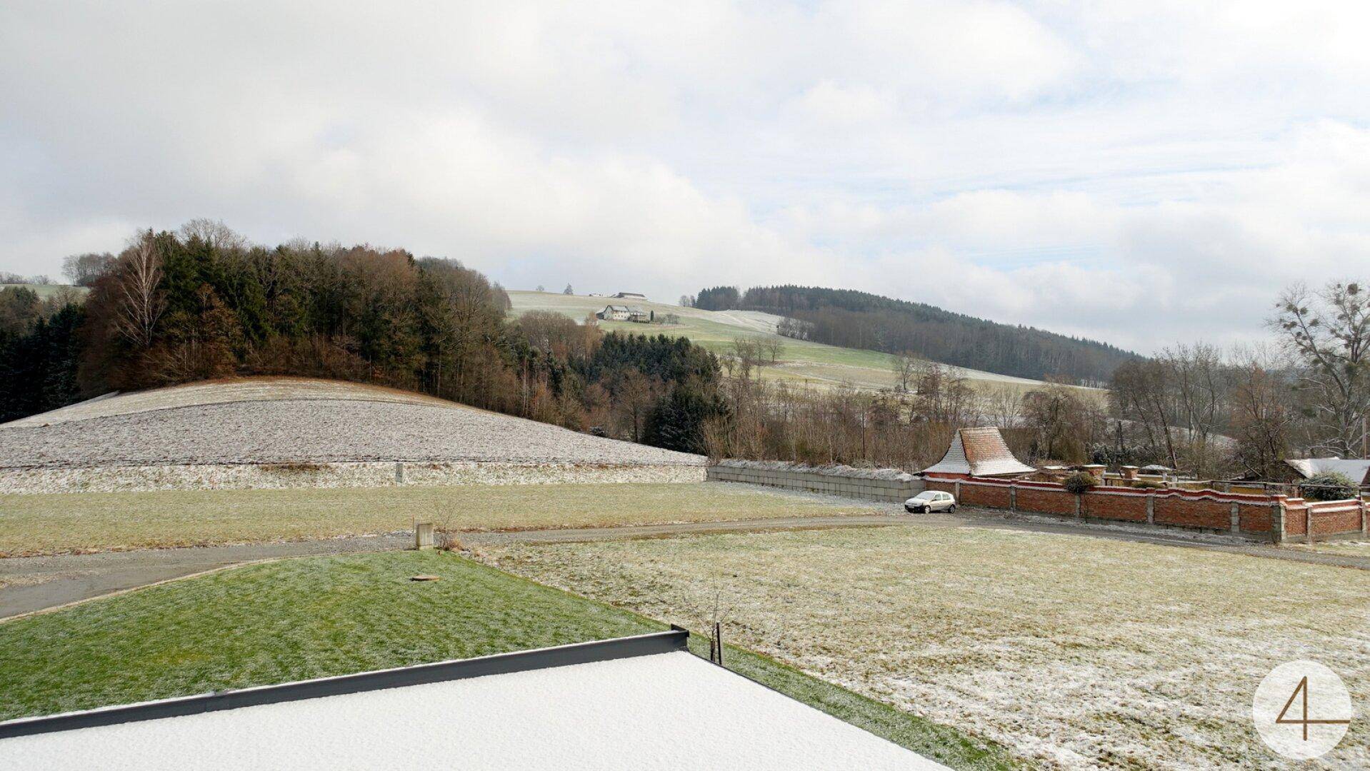 Weitläufiger Blick über verschneite Felder und bewaldete Hügel in ländlicher Umgebung.