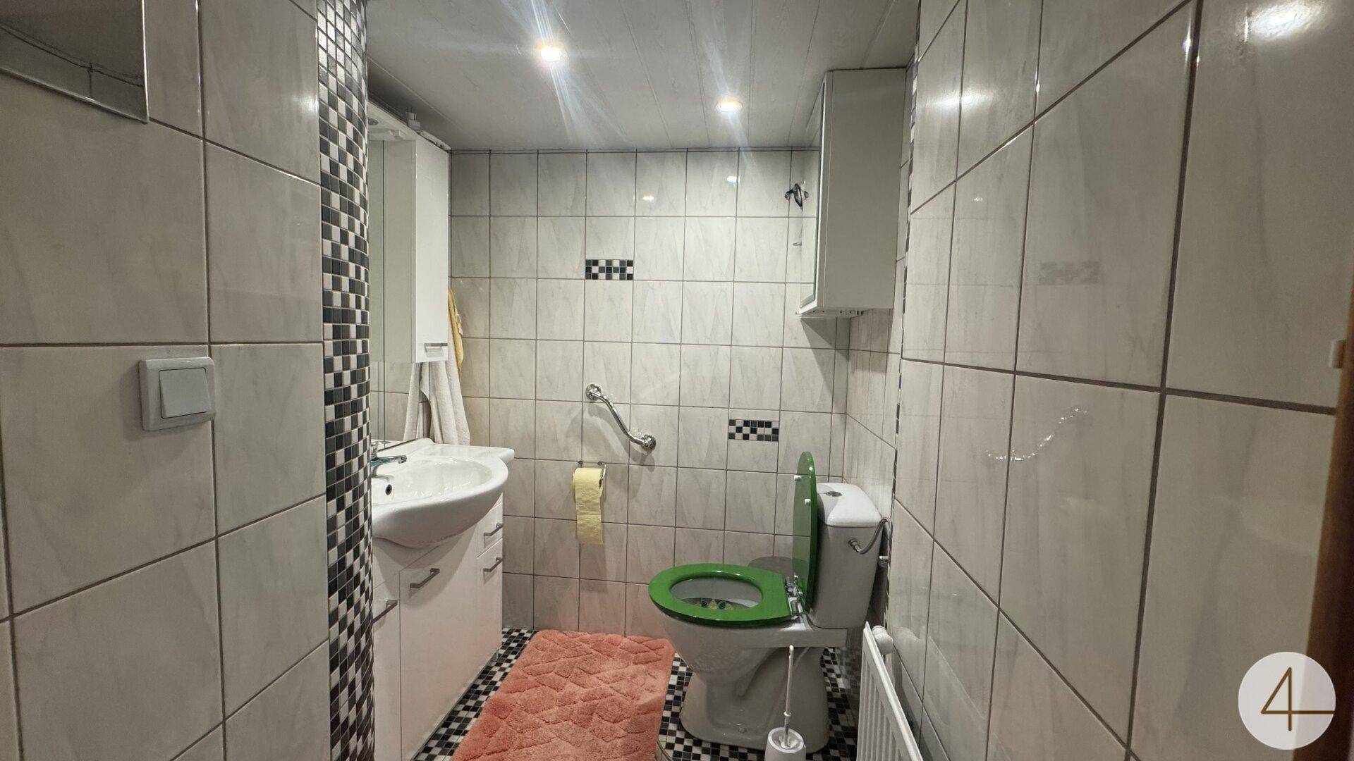 Kleines WC mit Waschbecken, Toilette und Haltegriffen, hell gefliest und funktional.