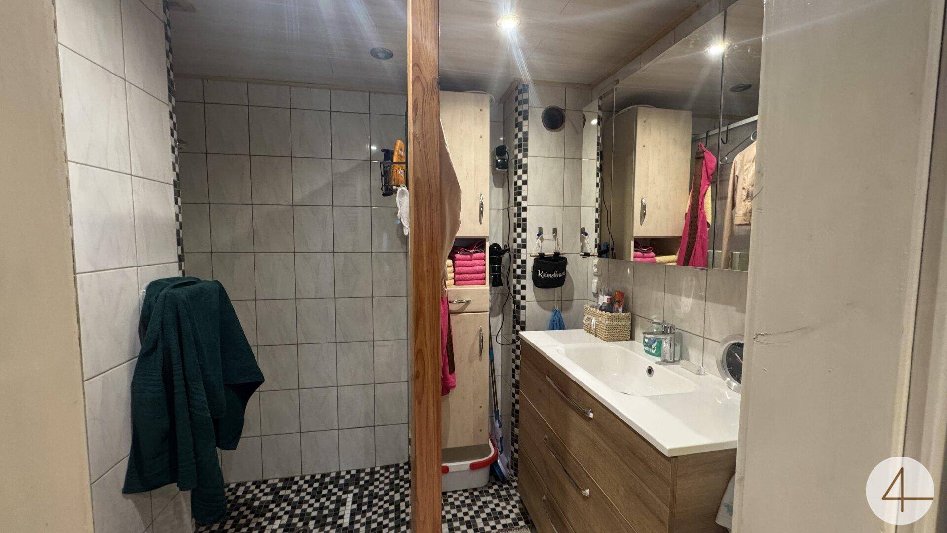 Funktionales Badezimmer mit Duschbereich, Waschbecken und Spiegelschrank, hell gefliest.