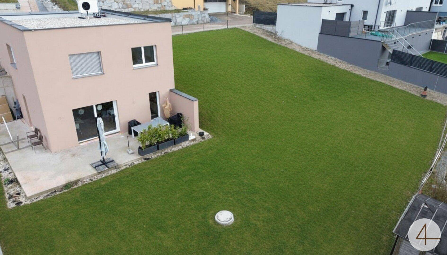 Luftaufnahme eines modernen Hauses mit großer Rasenfläche und kleiner Terrasse.