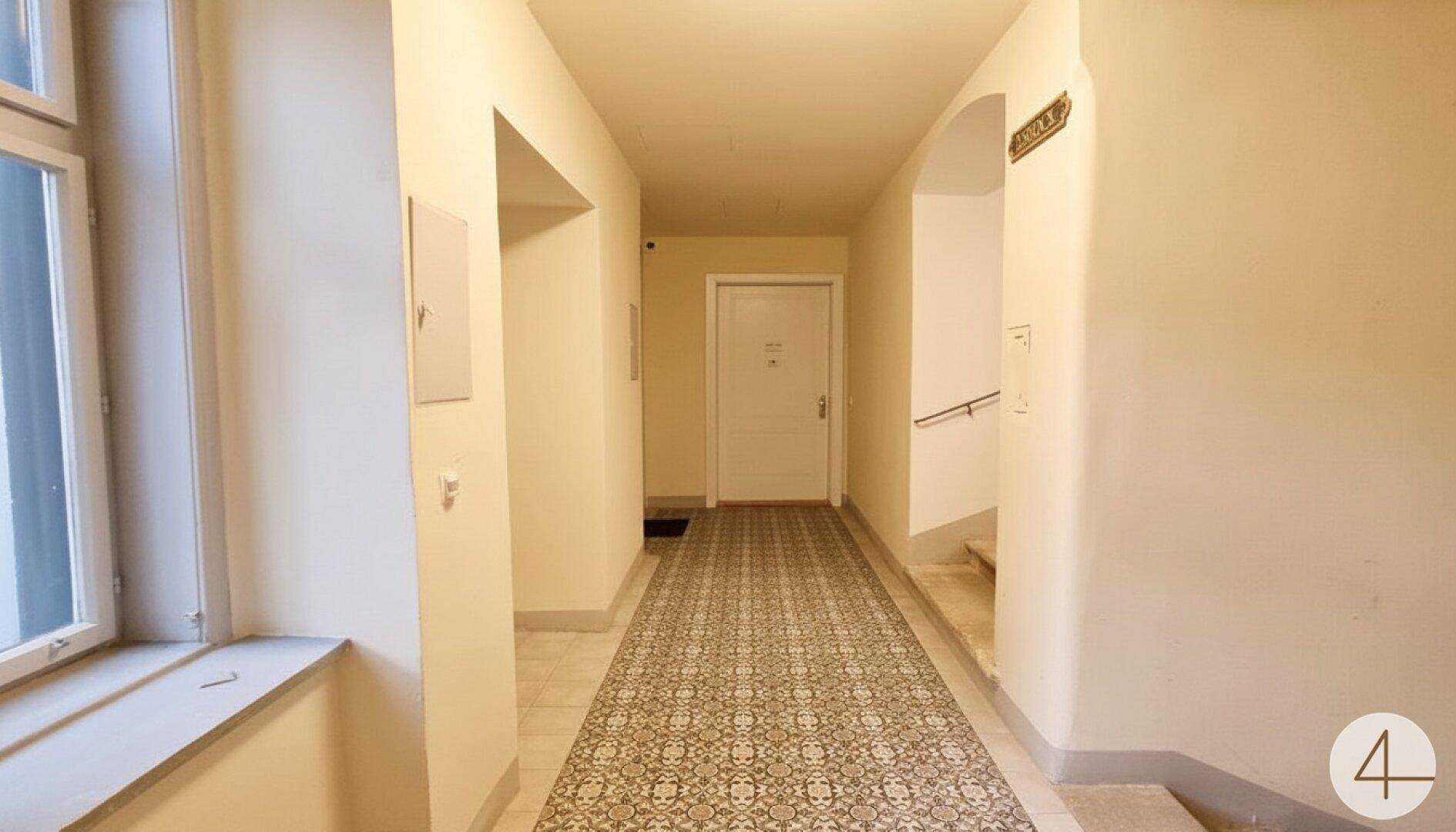 Eingangsbereich mit dekorativem Fliesenboden, hellem Anstrich und Zugang zum Treppenhaus.