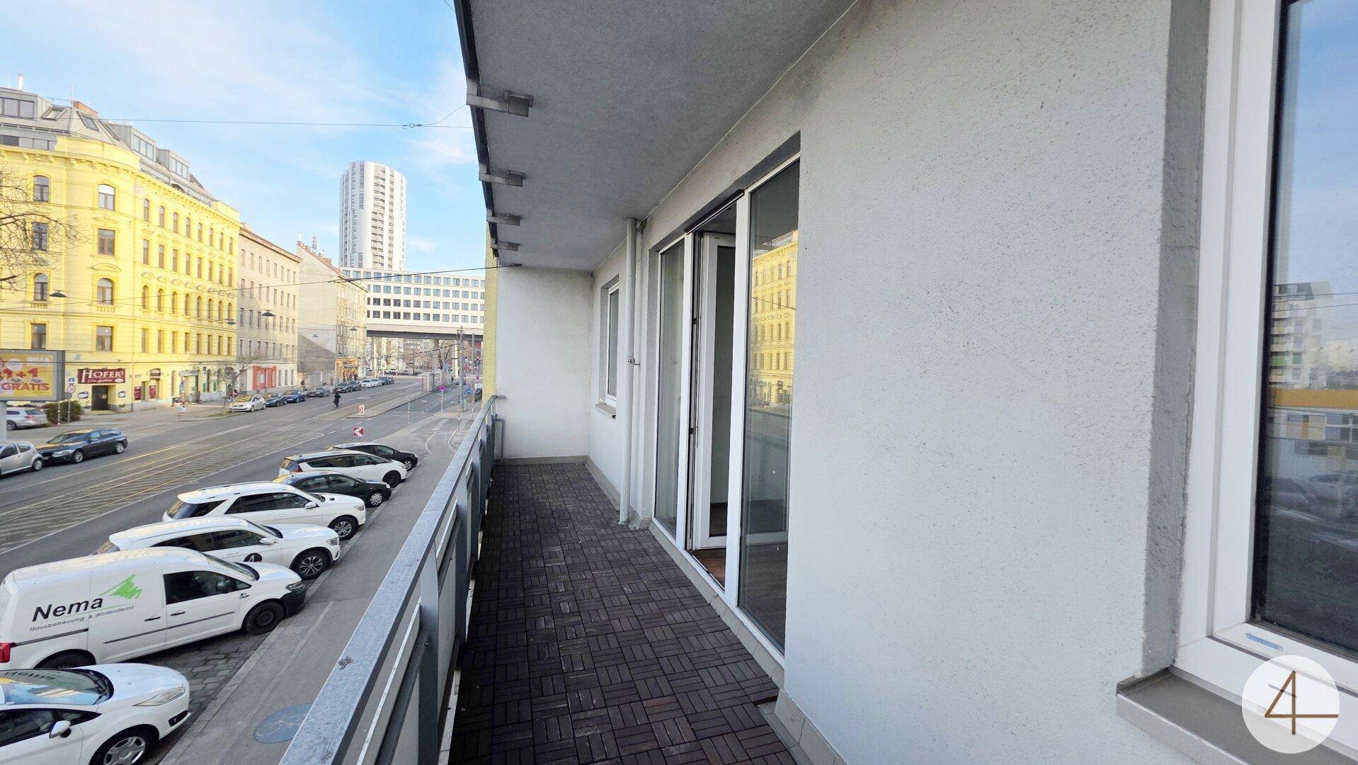Langer Balkon mit Blick auf die Stadtstraße und umliegende Gebäude, ideal für Entspannung im Freien.