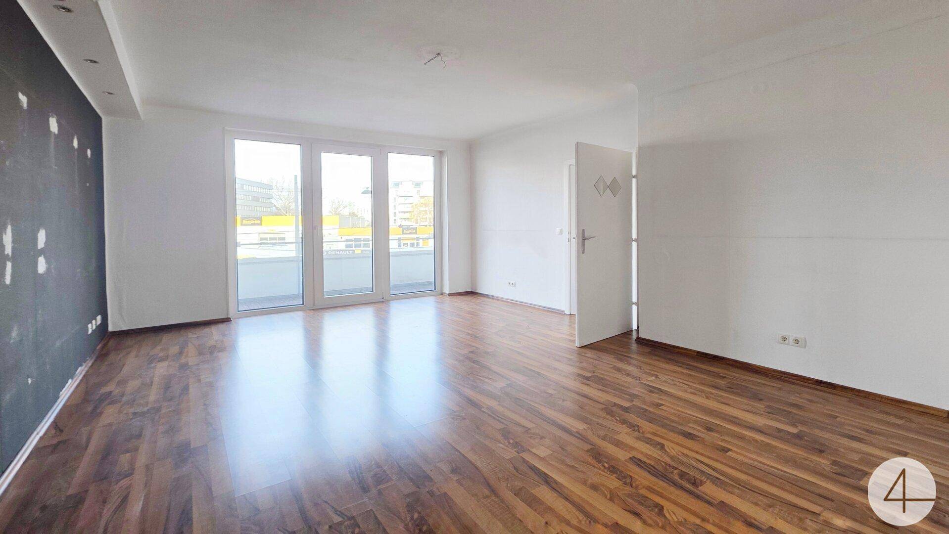 Geräumiges Wohnzimmer mit Laminatboden und großen Fenstern, die viel Tageslicht hereinlassen.
