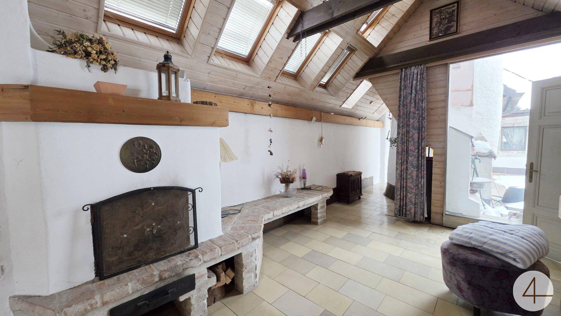 Heller Wohnbereich im Dachgeschoss mit Kamin, Fliesenboden, sichtbaren Holzbalken und Dachfenstern.
