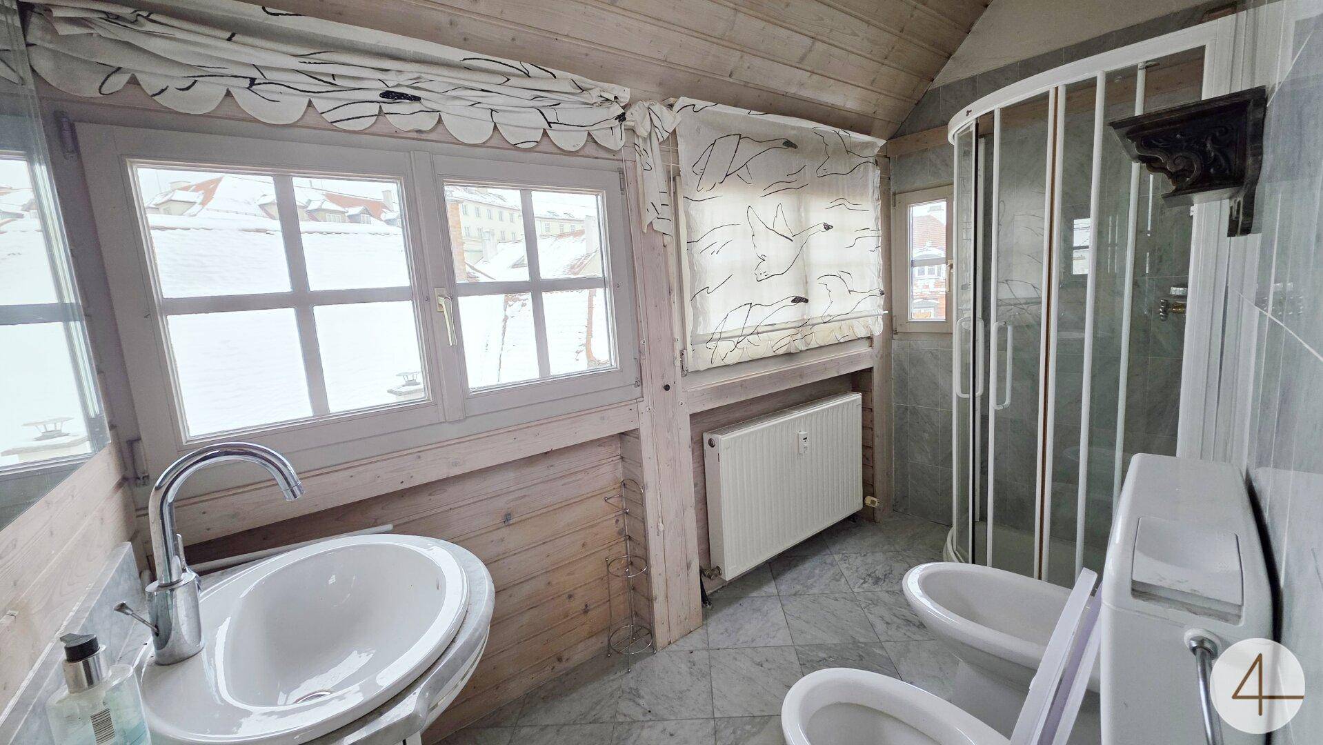 Badezimmer im Dachgeschoss mit Dusche, Waschbecken, WC, Bidet und Fenster mit Blick nach draußen.