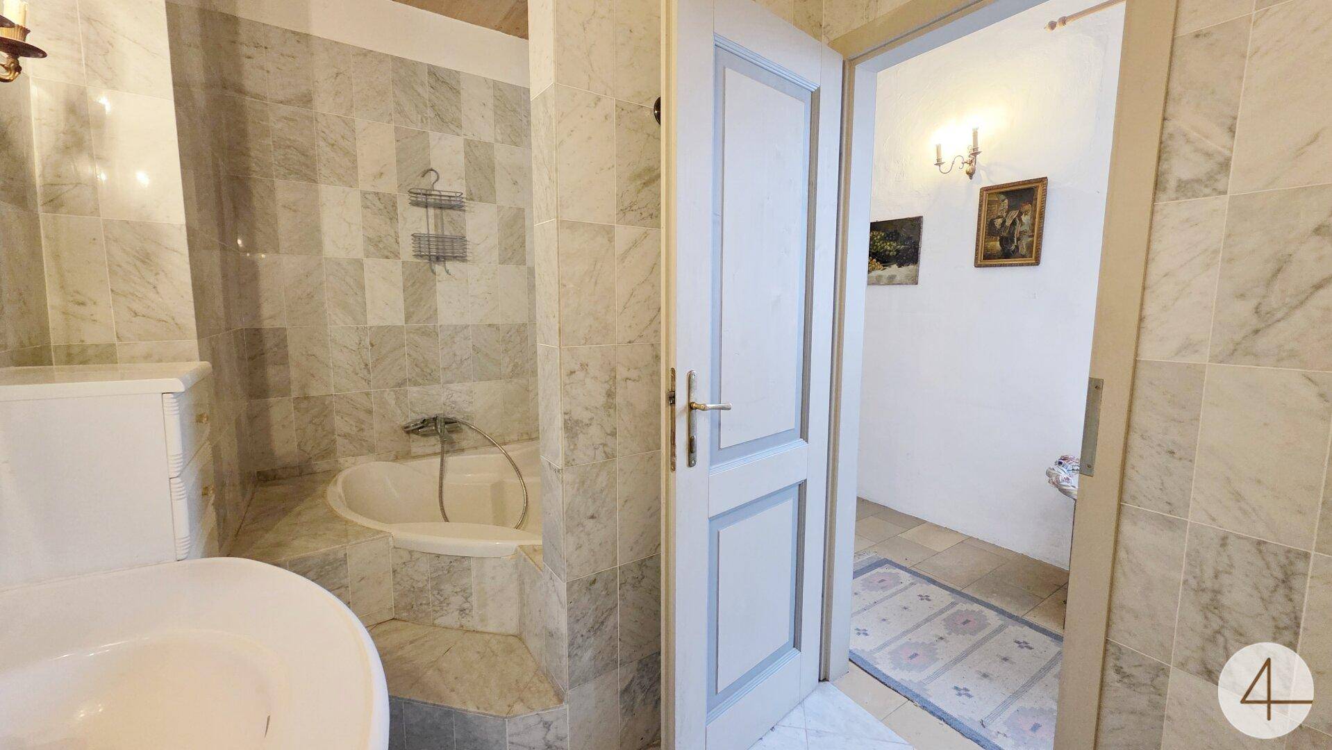 Badezimmer mit Badewanne, WC und eleganten Marmorfliesen an Wänden und Boden.