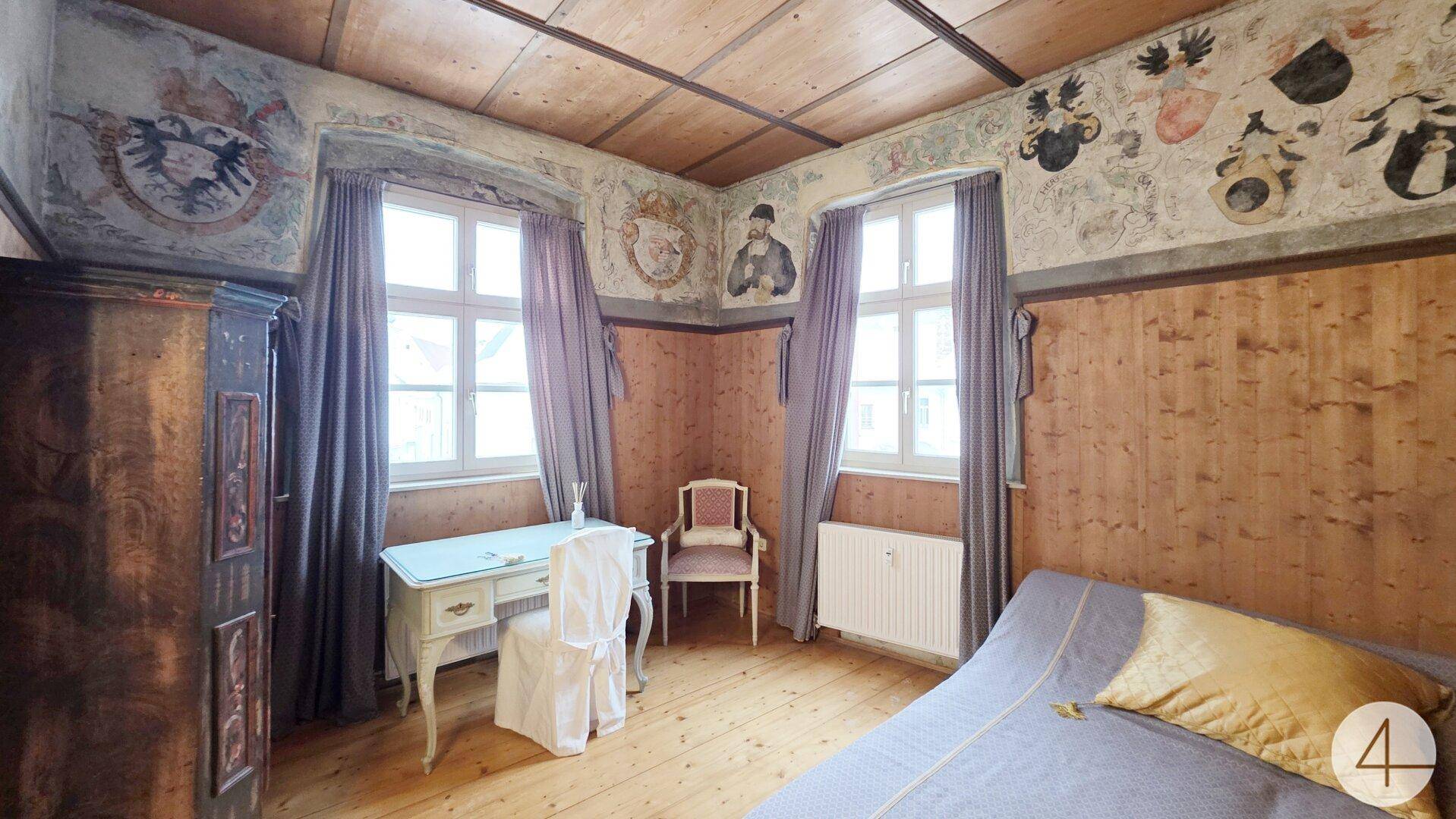 Schlafzimmer im historischen Stil mit Holzwänden, bemalter Decke und zwei Fenstern.