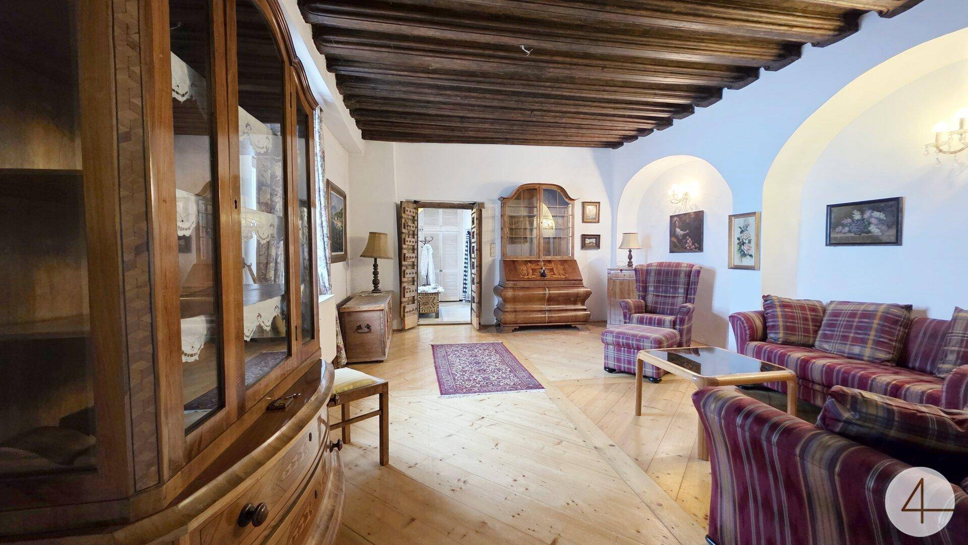 Großzügiges Wohnzimmer mit antiken Holzmöbeln, karierten Sofas und sichtbarer Holzbalkendecke.
