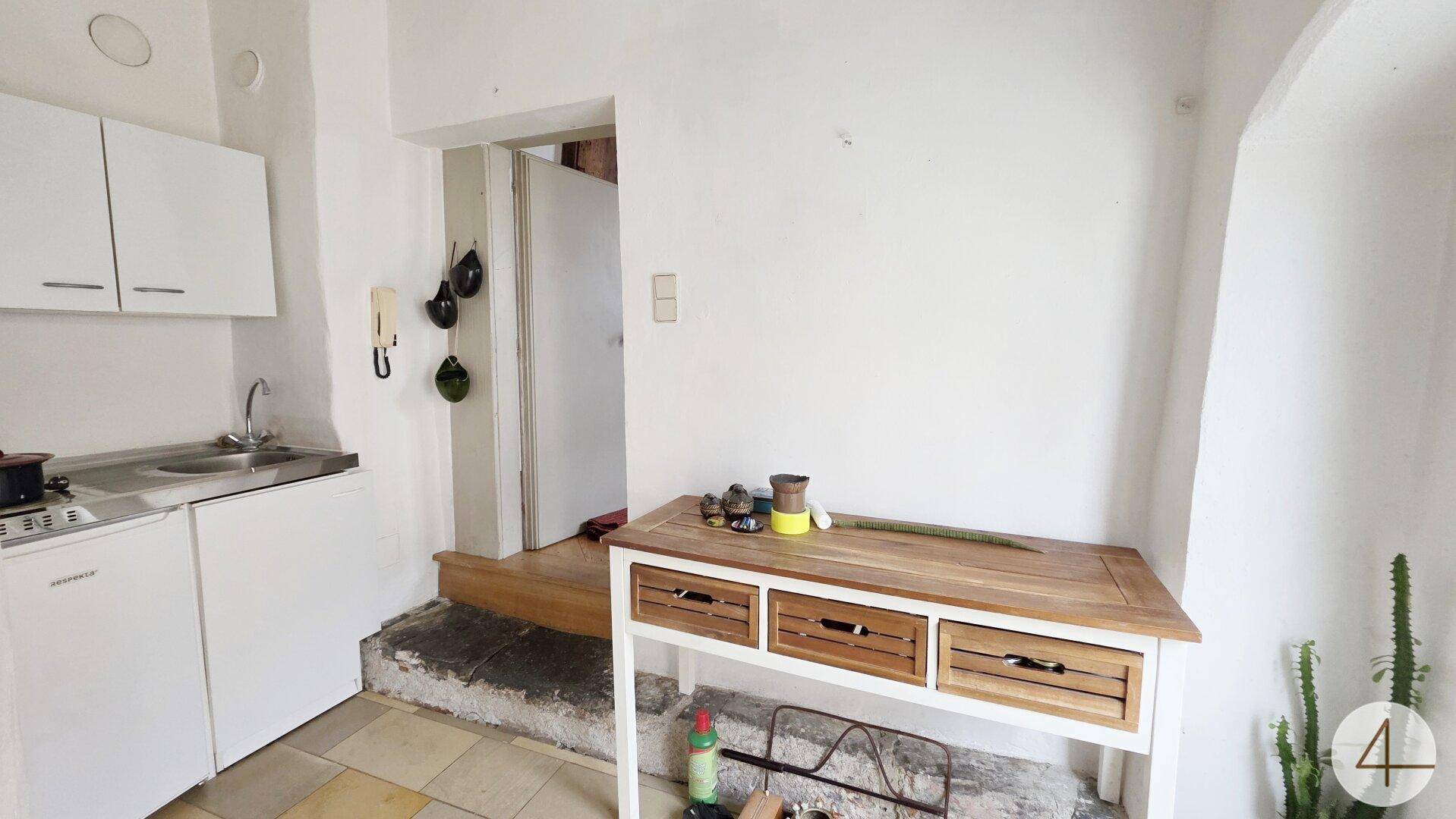 Kleine Küchenzeile mit Spülbecken, Kochfeld und Kühlschrank in einem einfachen Raum.